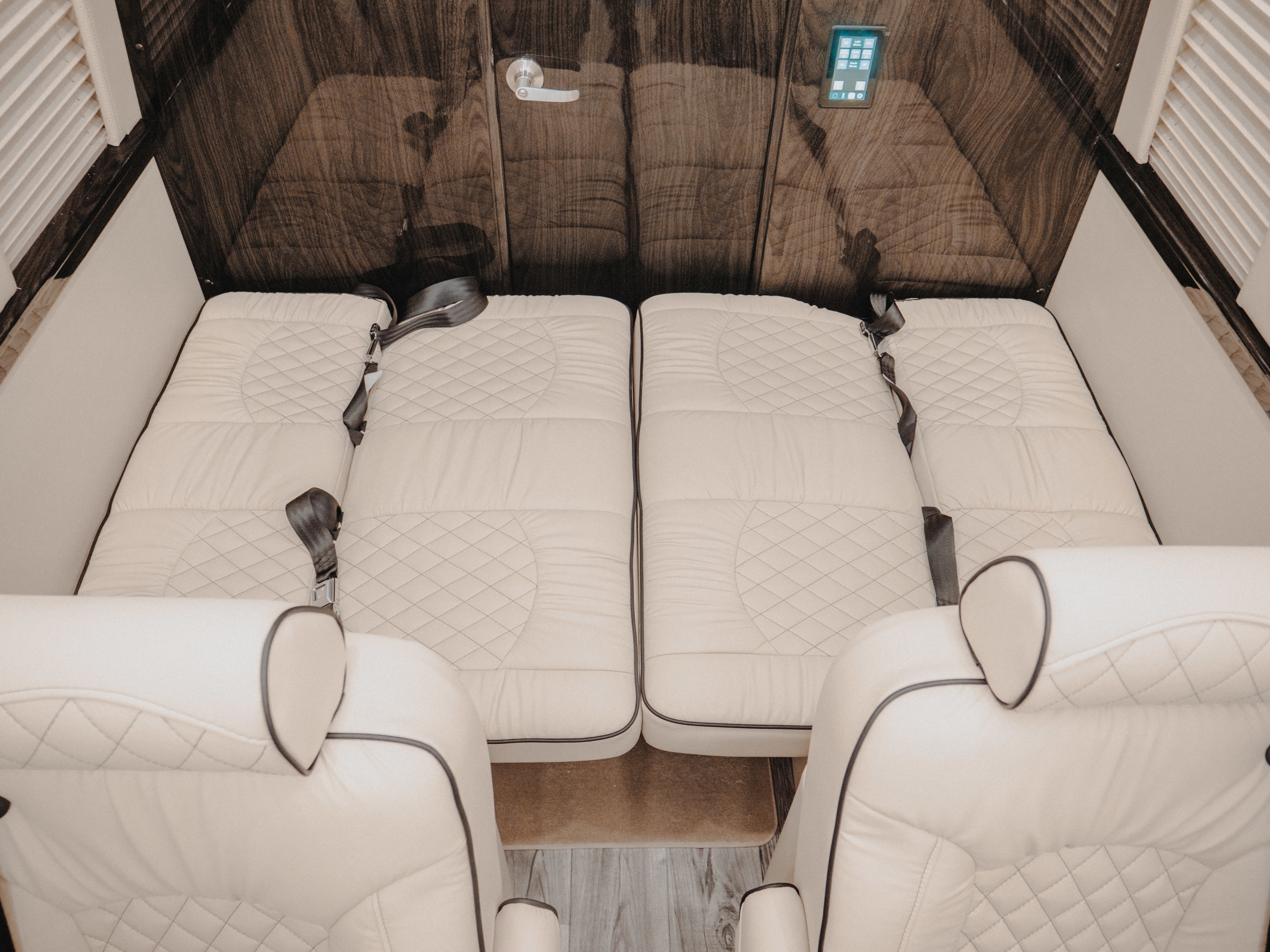 This RV rental interior features cream quilted beds with safety belts, alongside two plush seats, offering luxury and comfort.. Midwest Automotive Designs Midwest Automotive Designs Class B 2021