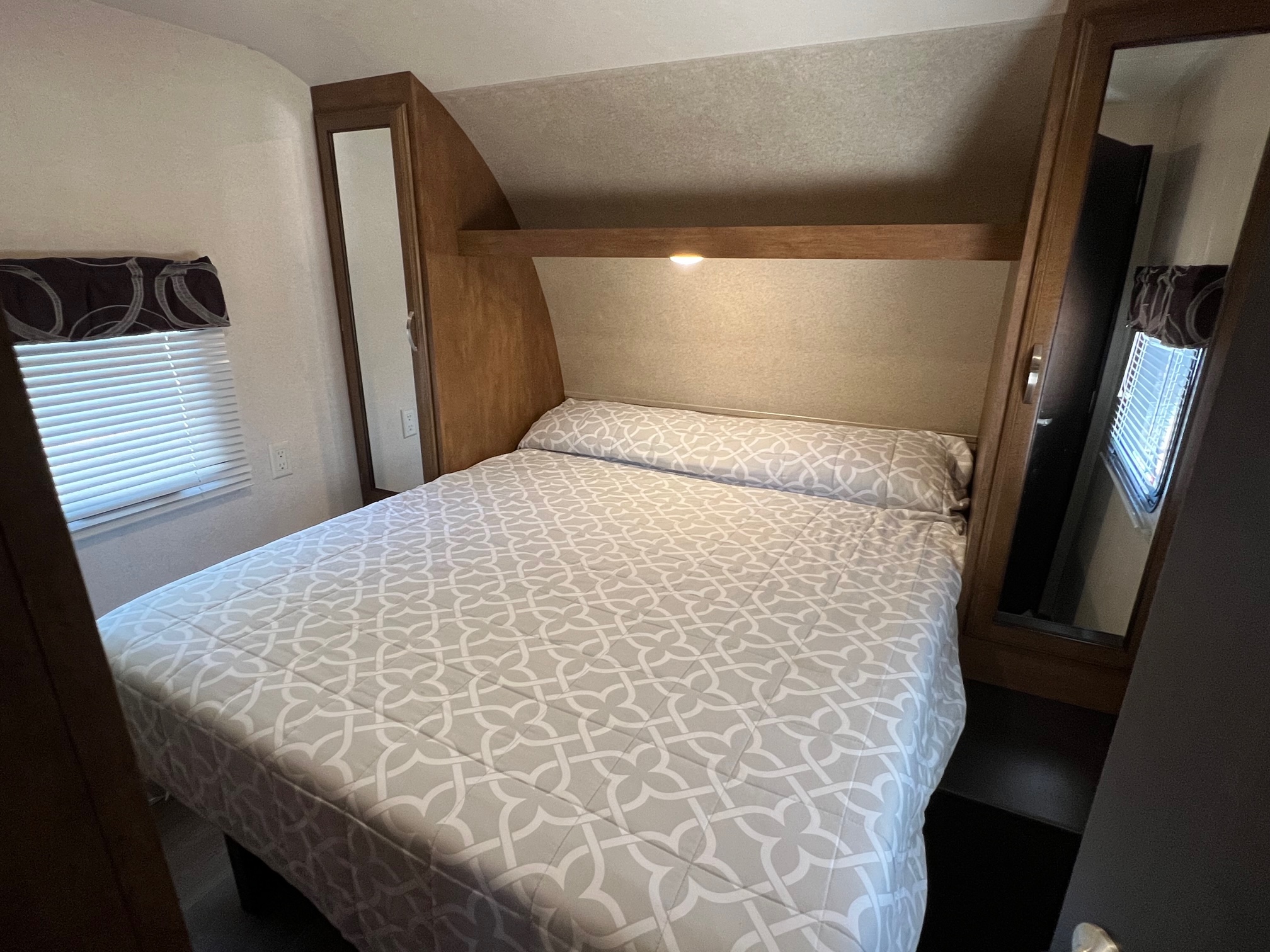 An RV rental bedroom shows a bed with a light gray patterned comforter, built-in storage, and a window with blinds.. Forest River Salem 2018