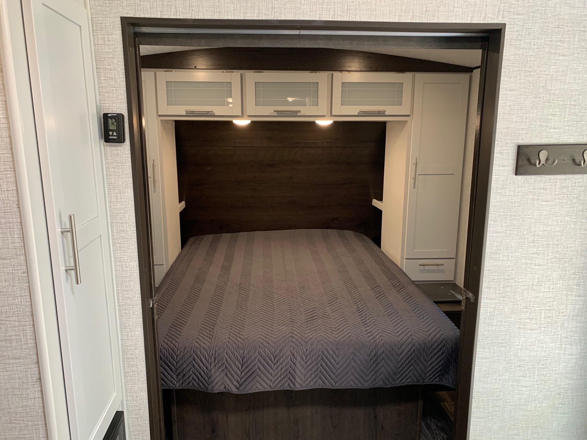 RV rental bedroom with full bed, overhead cabinets, and thermostat. Compact design for comfortable travel.. Keystone Bullet 2021