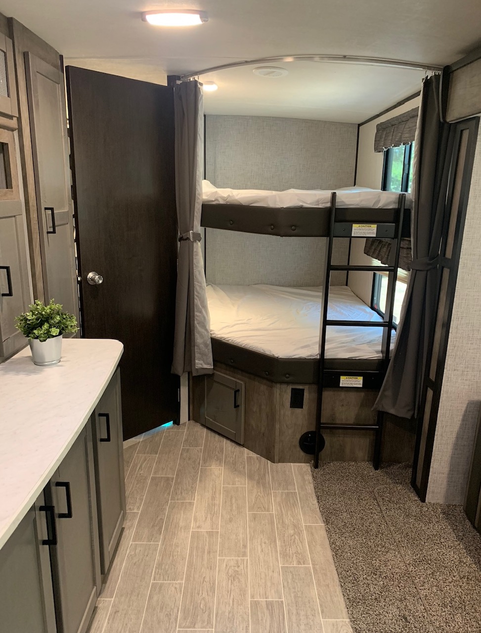 RV rental's interior: comfy bunk beds with ladder, privacy curtains, and a compact living area with diverse flooring.. Heartland Wilderness 2020
