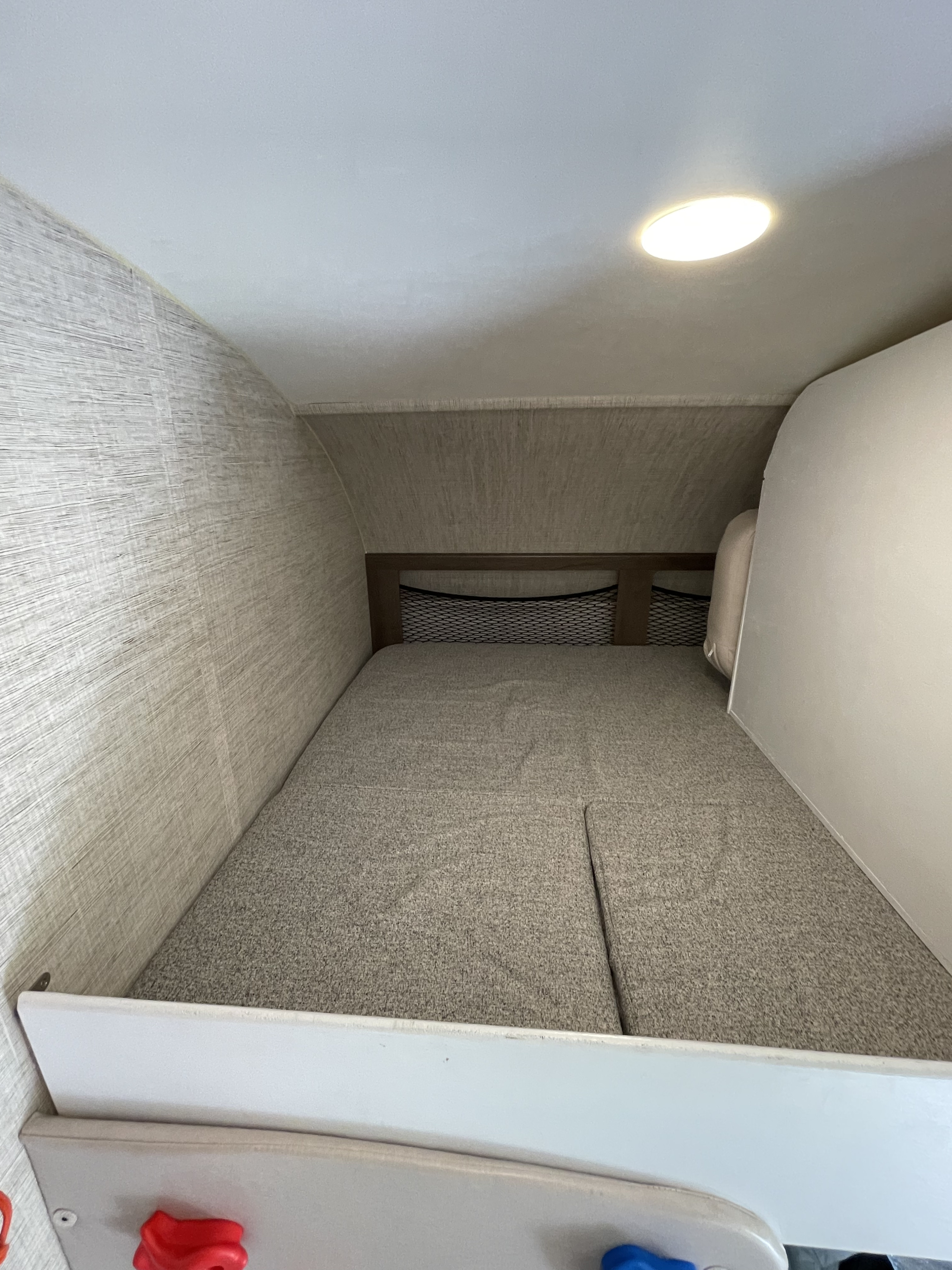 RV rental interior: a light-colored, textured sleeping bunk with a mesh headboard and bright ceiling light.. Jayco Redhawk 2021