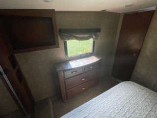 Inside an RV rental bedroom: a cozy bed, dresser below a window, and built-in storage. Ideal for travel comfort.. K-Z Manufacturing Durango 2014