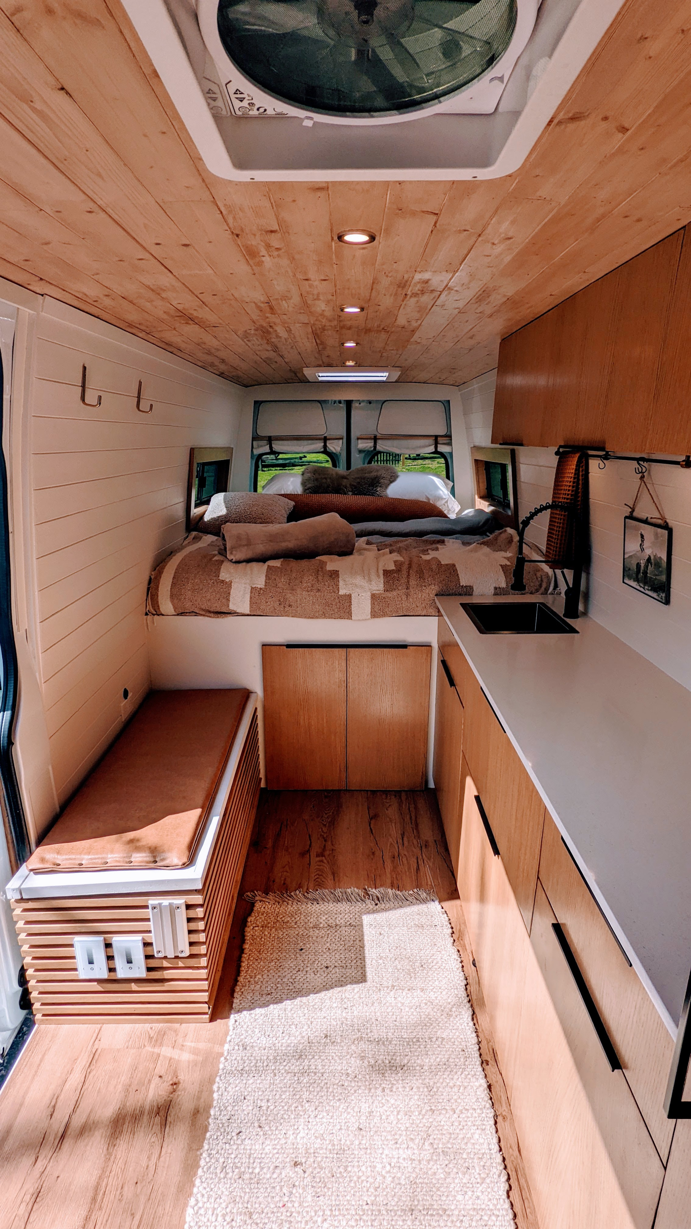Cozy rv rental interior featuring a wood ceiling, shiplap walls, compact kitchen, and a comfy bed. Perfect for van life adventures!. Mercedes-Benz Sprinter 2020