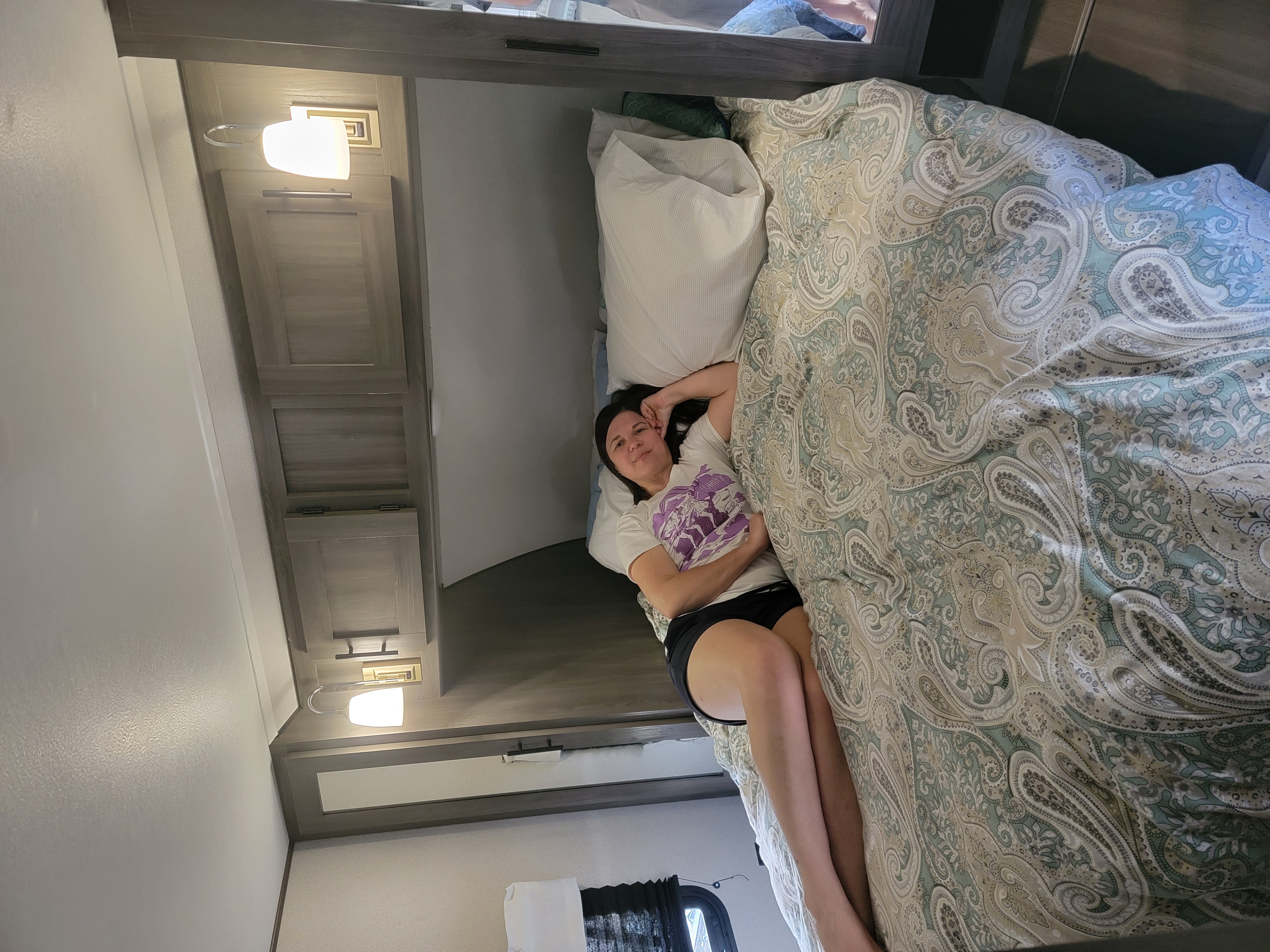 Enjoying the comfort of an RV rental: a woman relaxes on a bed with a paisley comforter in a cozy bedroom.. Forest River Shasta 2021