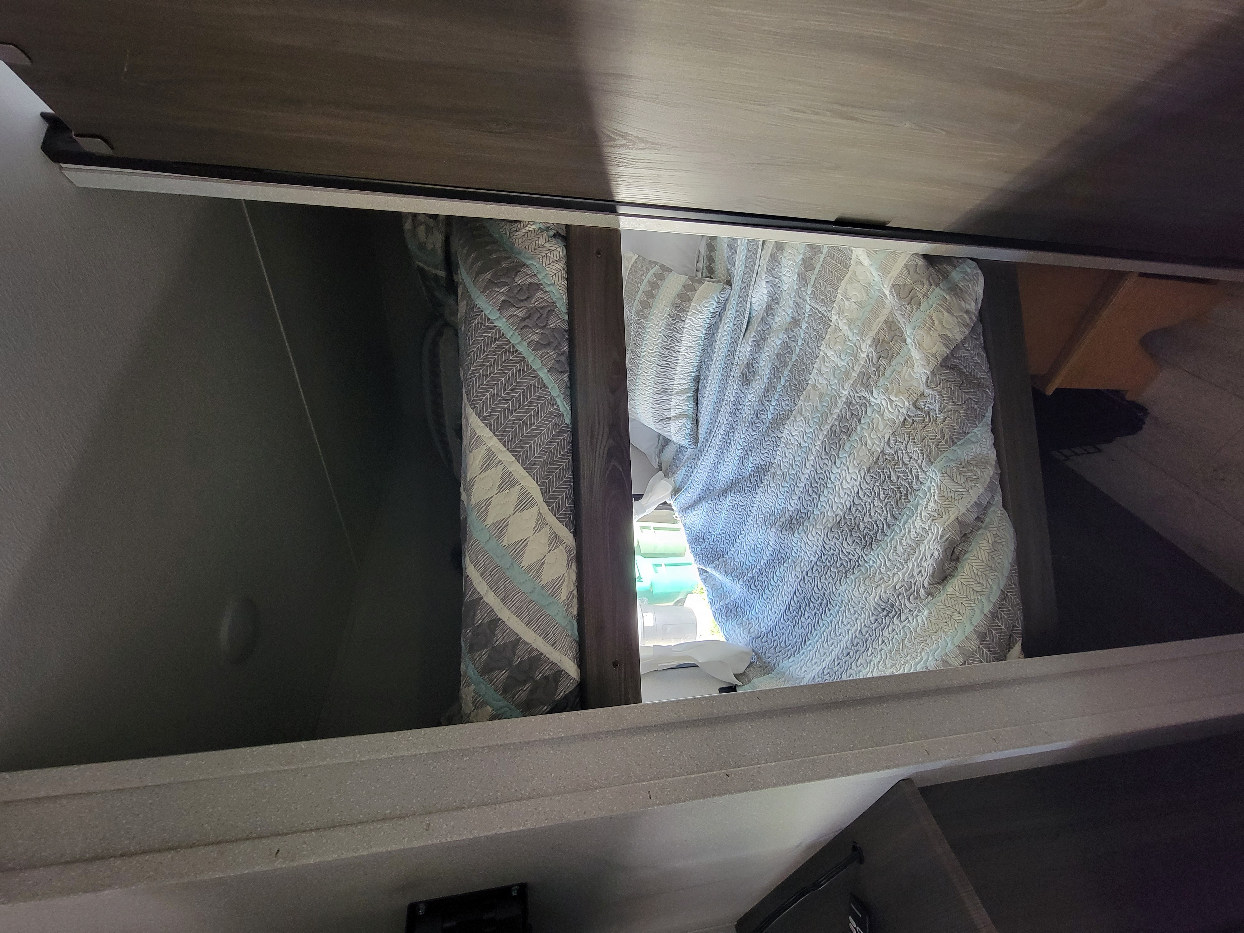 Inside an RV rental: a compact sleeping area with a patterned quilt. Ideal for travelers, offering cozy comfort and storage.. Forest River Shasta 2021