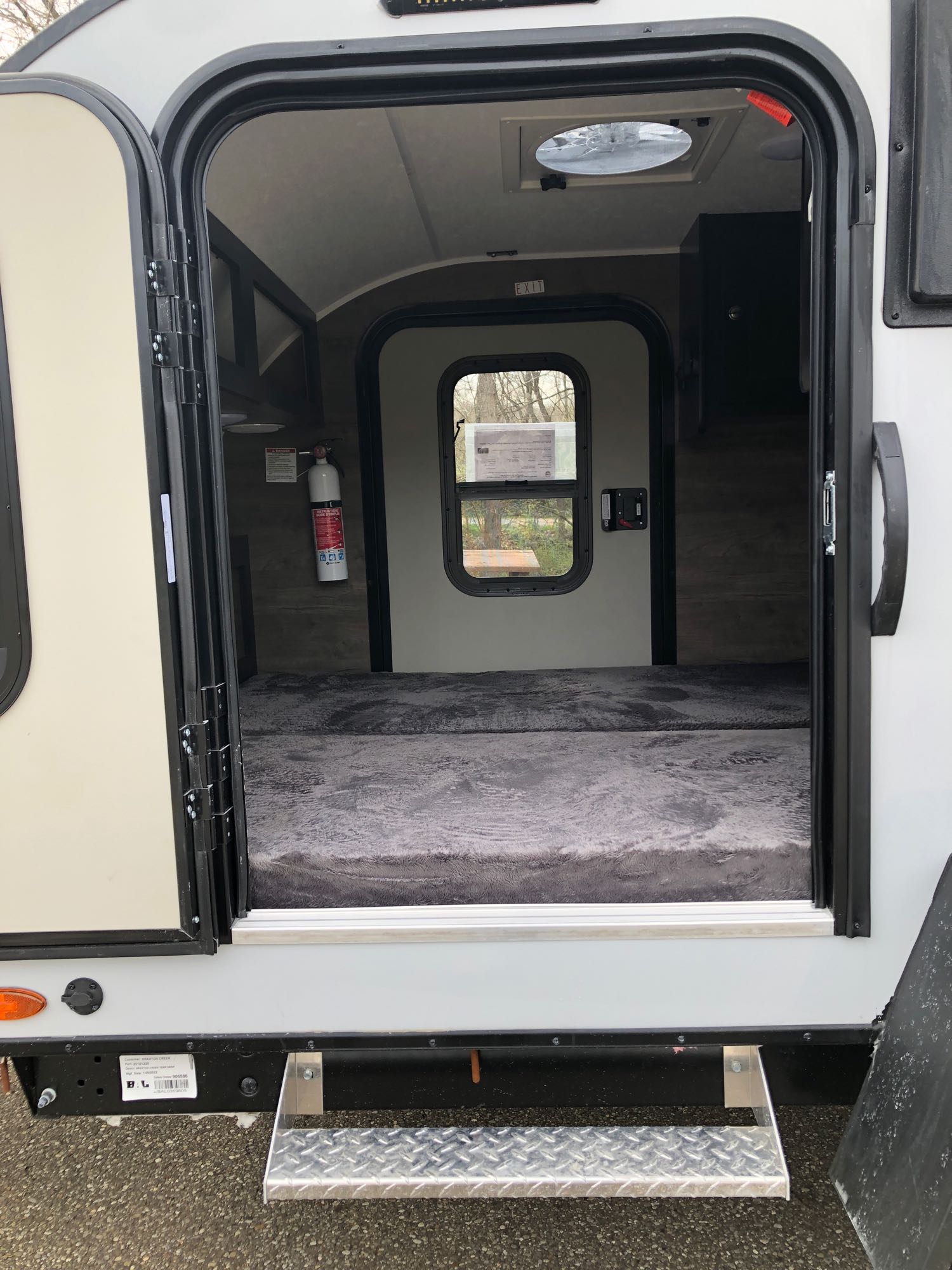 An open door shows the inviting interior of an RV rental, featuring a comfortable bed, fire extinguisher, and overhead vent.. Braxton Creek Bushwhacker 2022