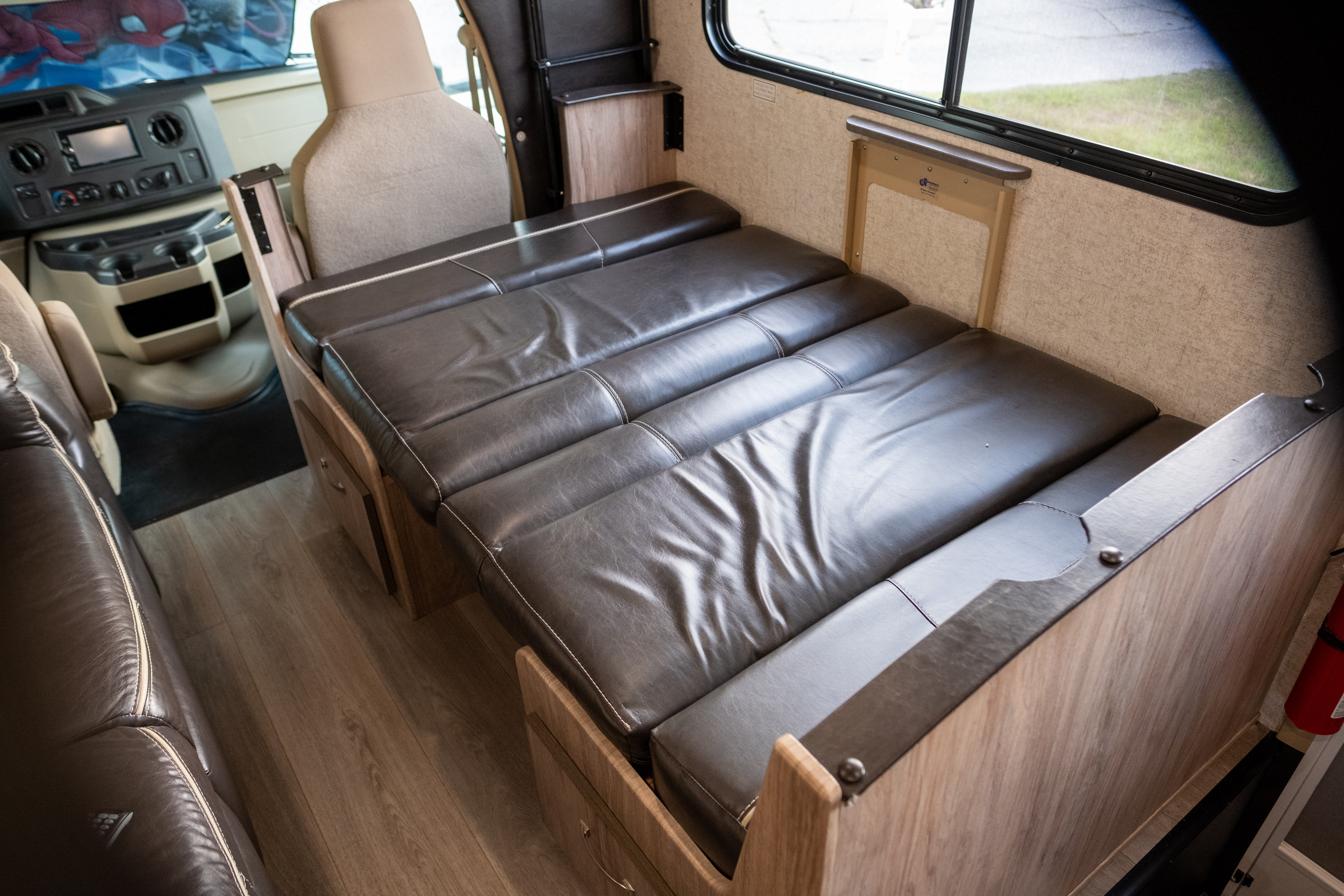 Inside an RV rental: a flexible brown leather dinette converts to a bed, with the driver's cockpit visible.. Forest River Sunseeker LE 2017