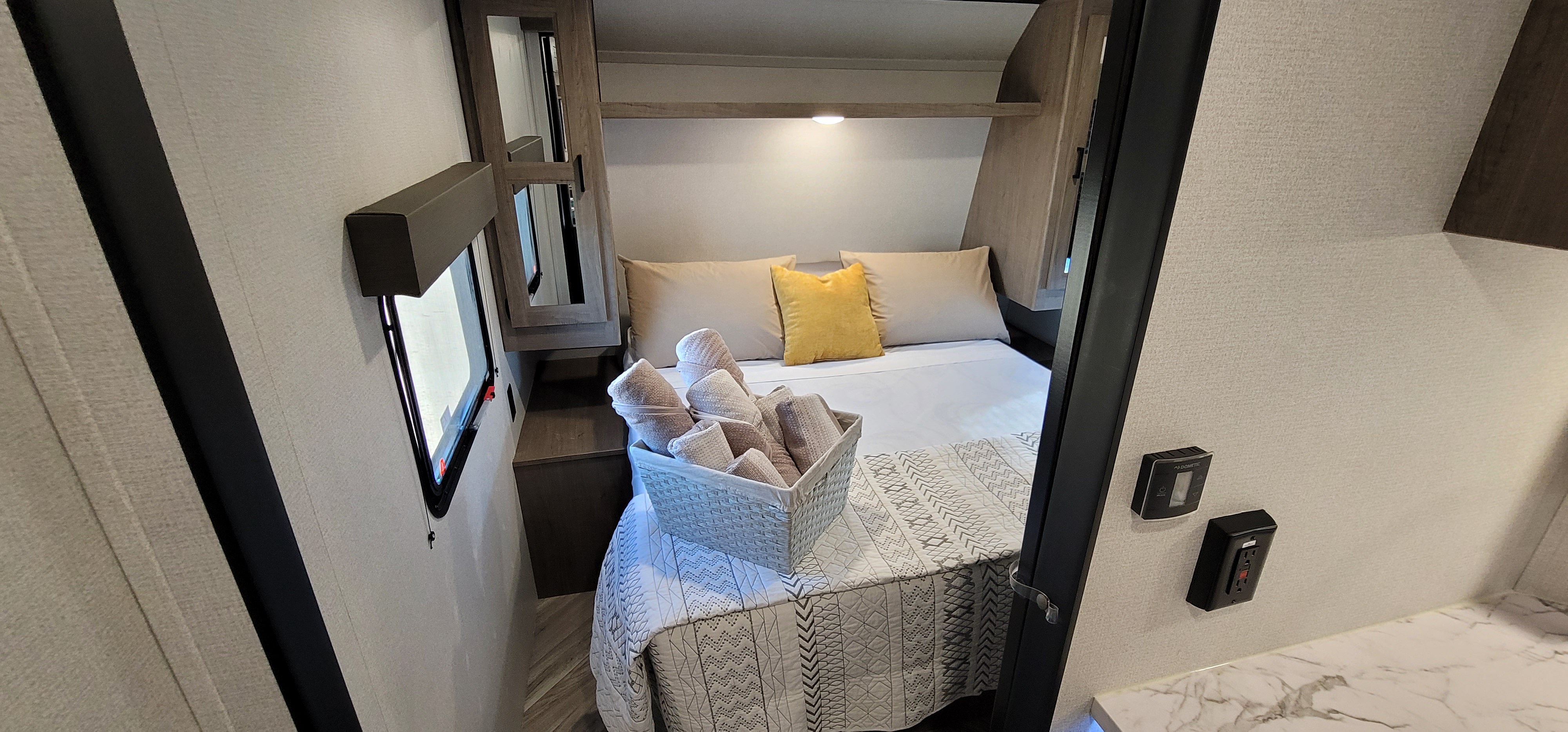 Cozy RV rental bedroom showcasing a comfortable bed with a yellow pillow, rolled towels, and convenient interior controls.. Keystone RV Hideout Luxury Edition 2021