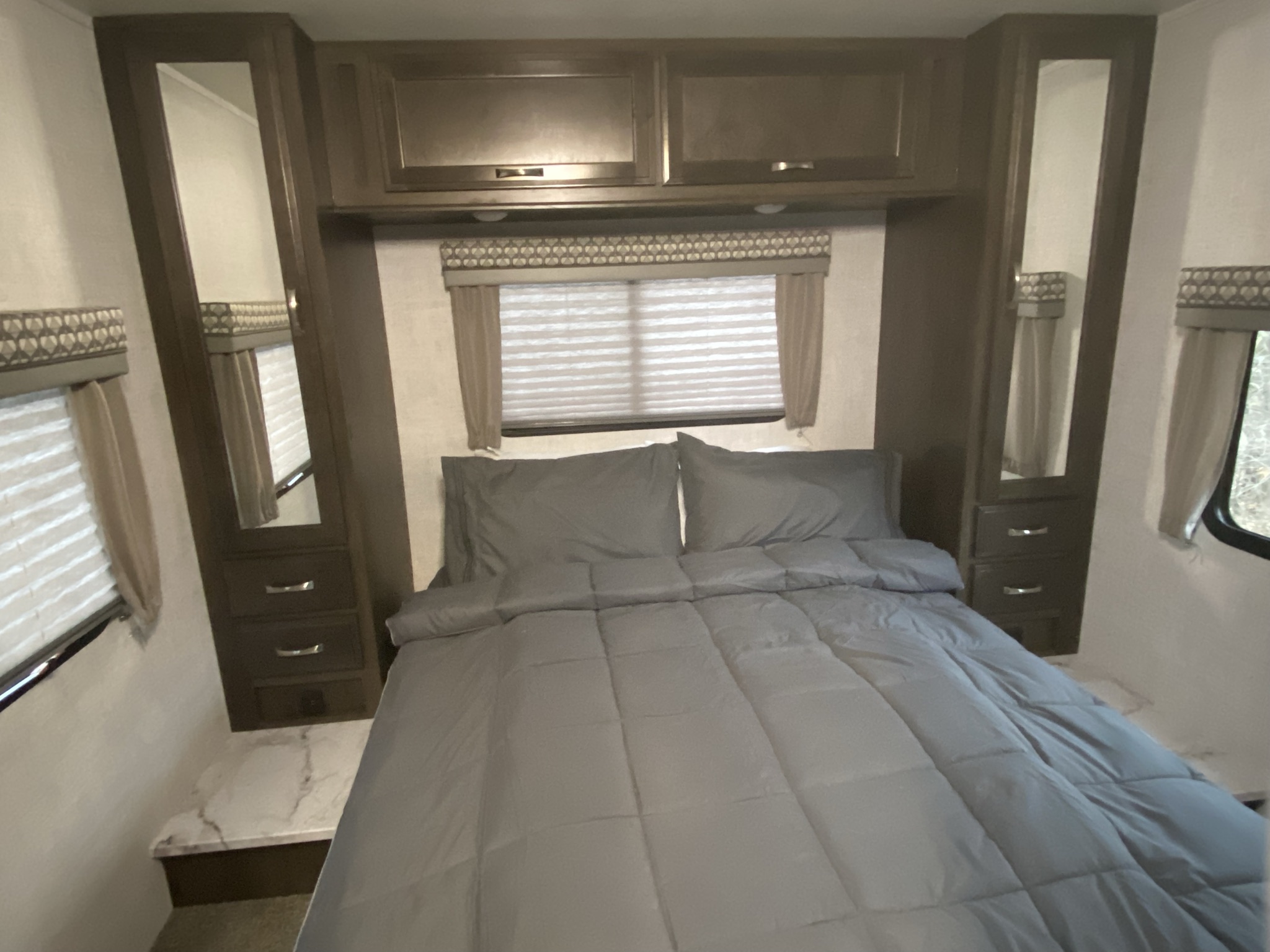 Cozy RV rental bedroom with a neat gray bed, overhead cabinets, and built-in side storage with mirrors.. Gulf Stream Conquest LE 2021