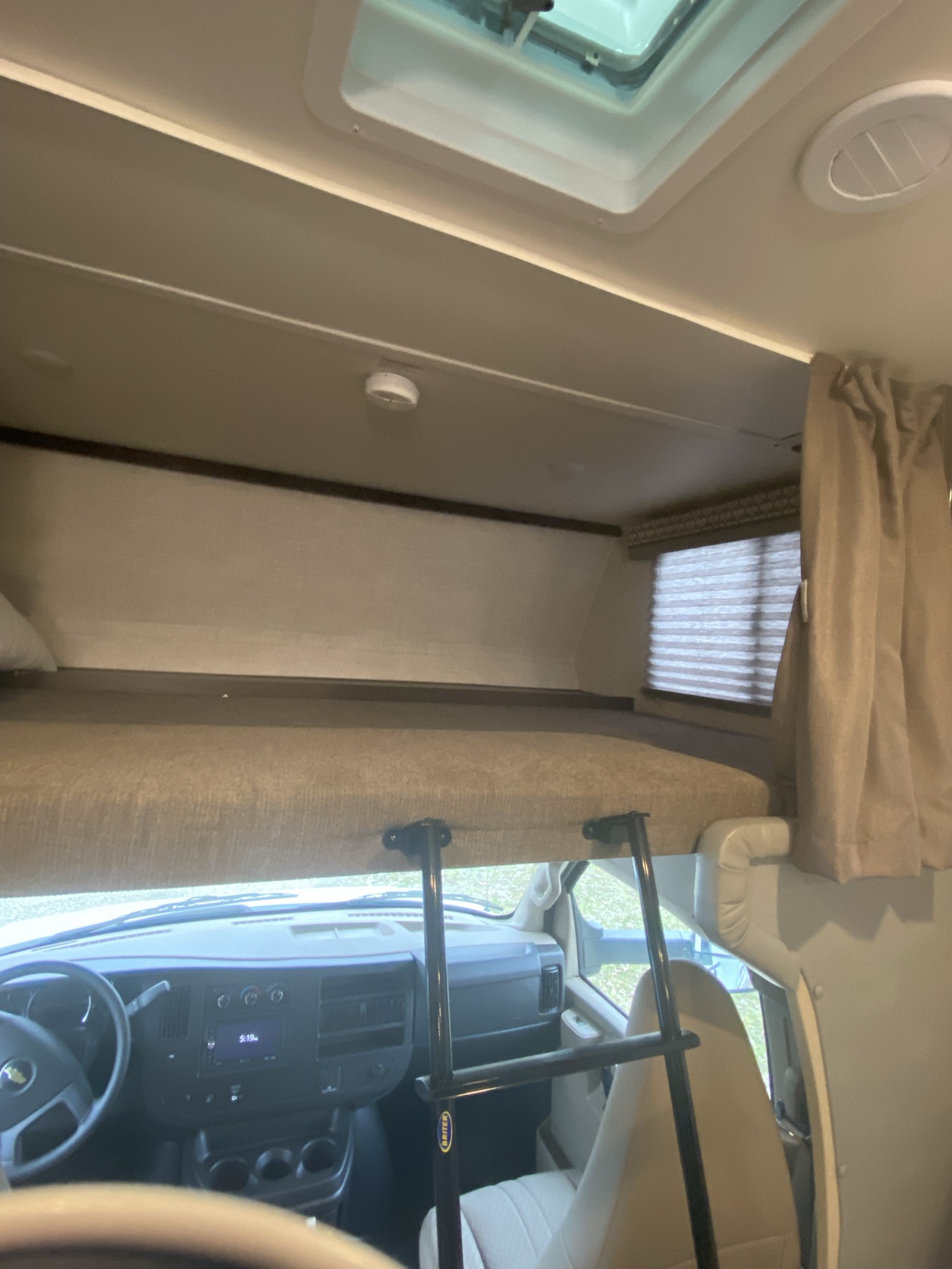 RV rental interior: A cozy overhead bunk with ladder overlooks the driver's cabin, including a dashboard and seats.. Gulf Stream Conquest LE 2021