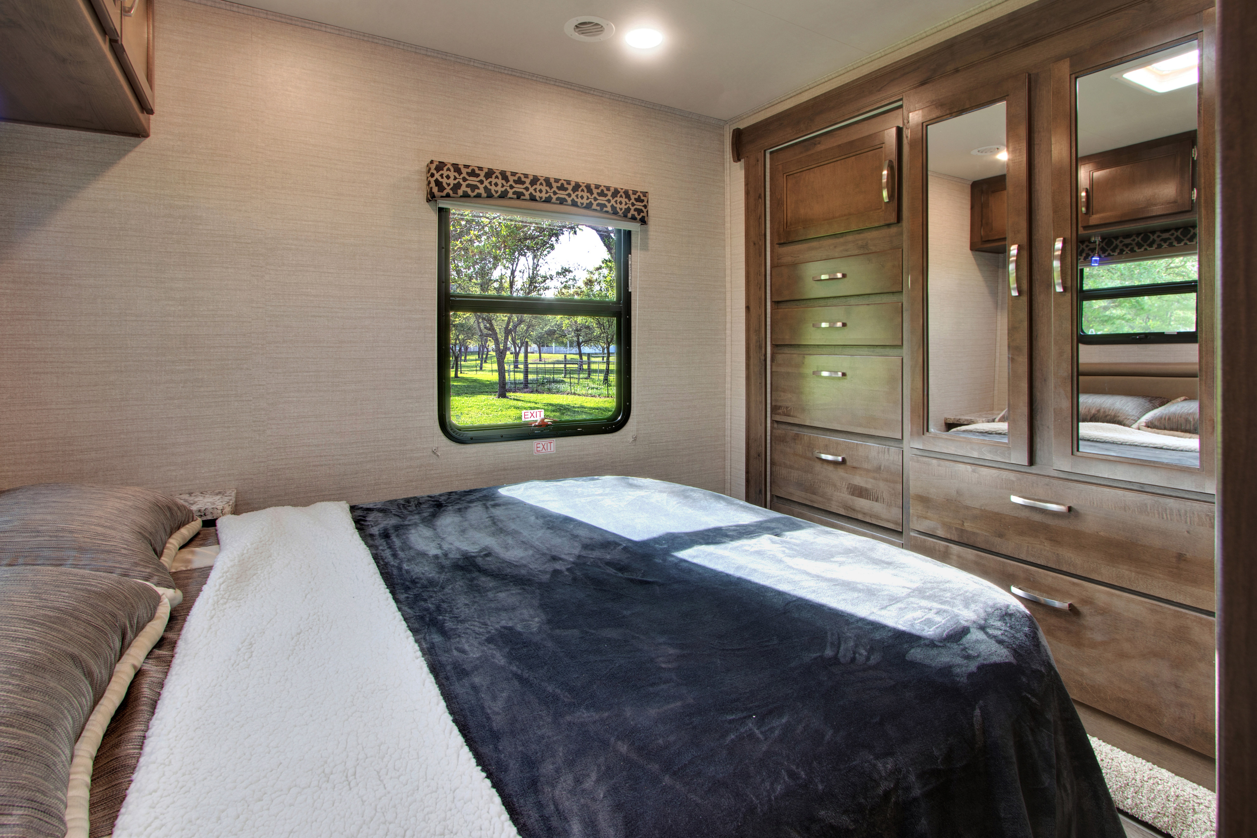 This RV rental bedroom offers a comfortable bed, window with a lush outdoor view, and mirrored closet/drawer storage.. Jayco Redhawk 2020