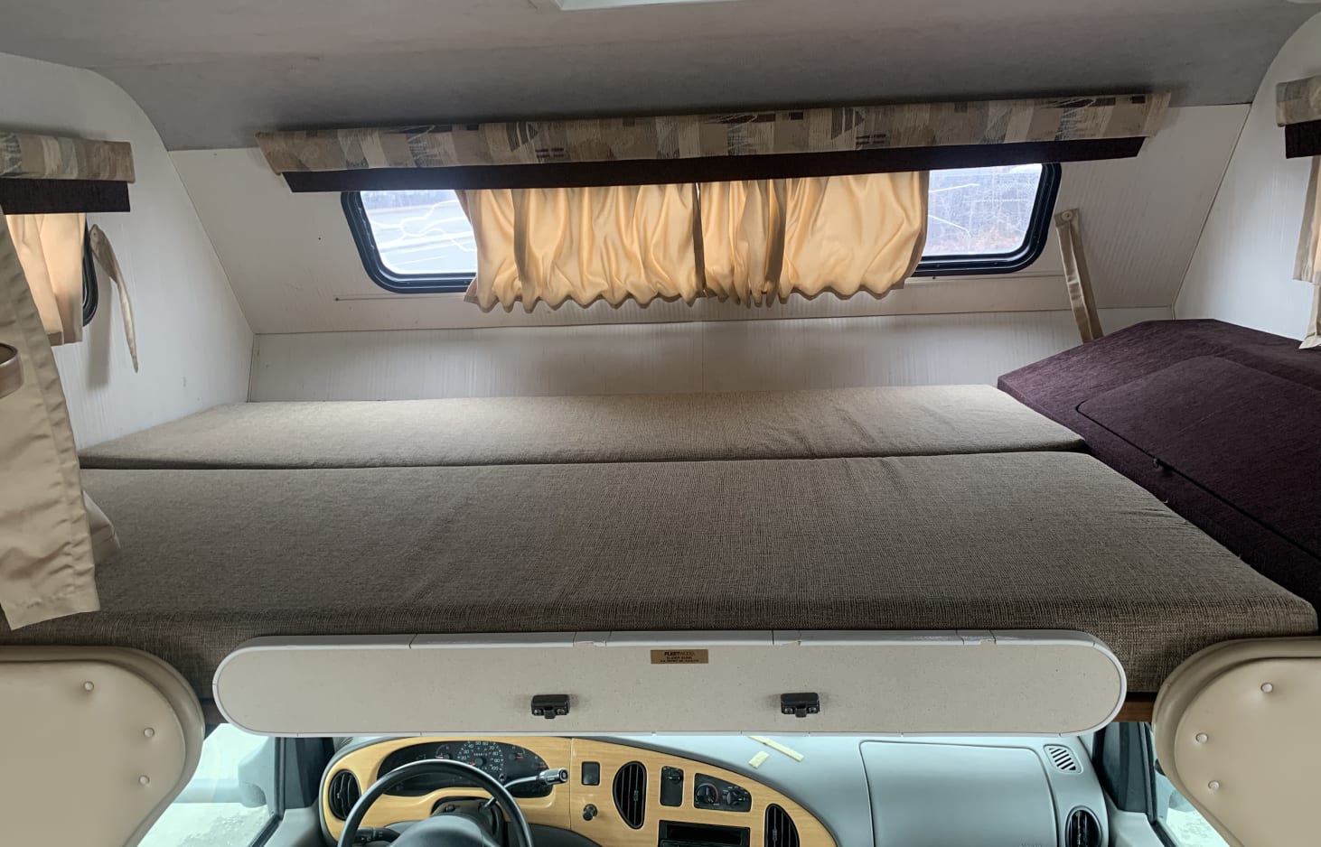 View of an RV rental's over-cab bunk bed with light mattresses, curtains, and dashboard below. Ready for your trip.. Tioga Tioga Motorhome 2000