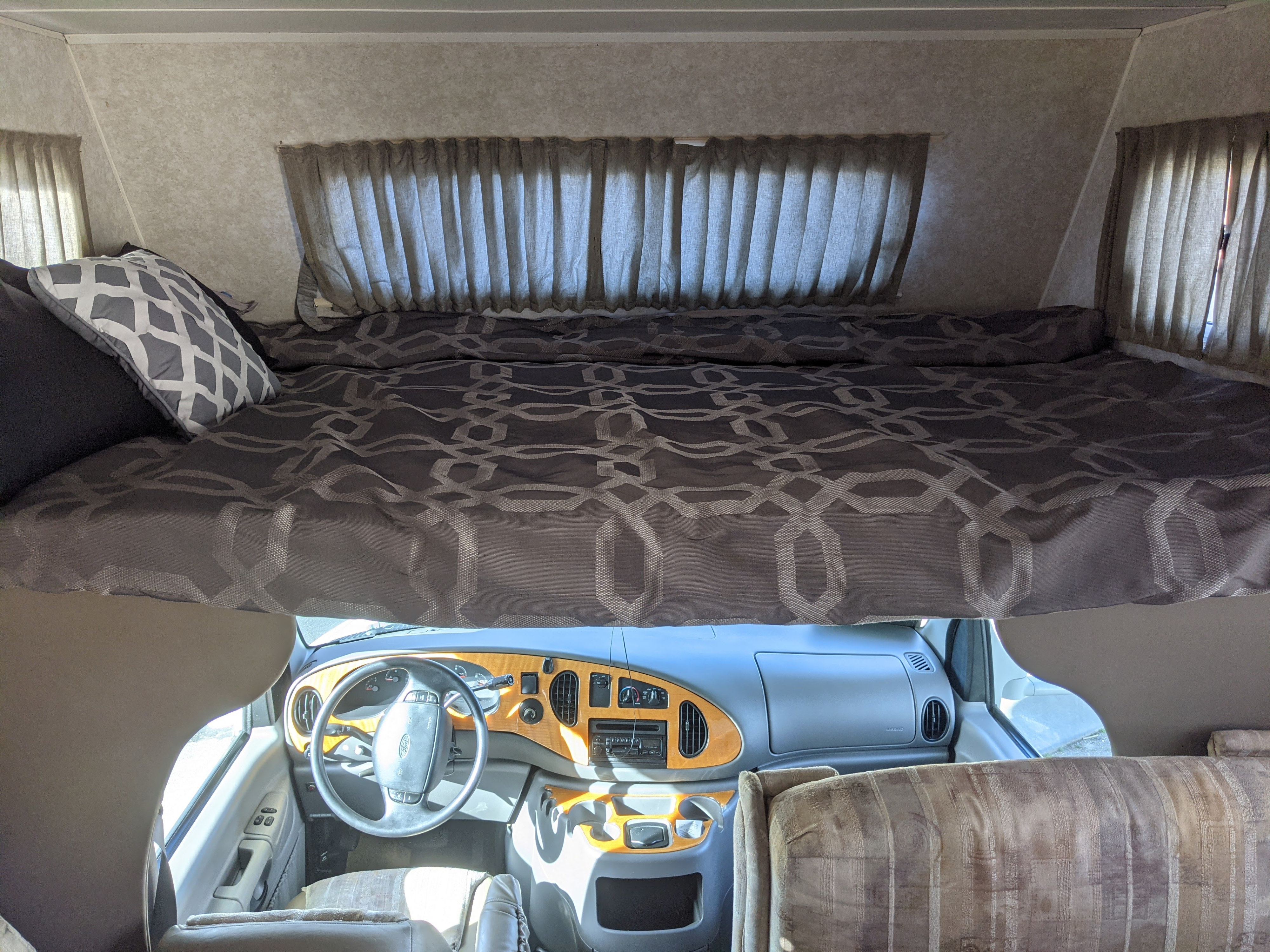 RV rental interior: A cozy cab-over bed with patterned linens sits above the driver's cockpit and dashboard.. Jayco Eagle 2001