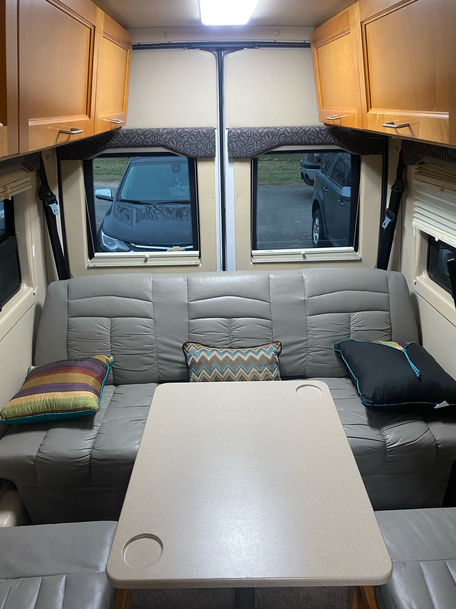RV rental interior: A cozy dinette setup with a plush sofa, center table, and large windows revealing parked cars outside.. Leisure Travel Vans Leisure Travel Vans Class B 2005