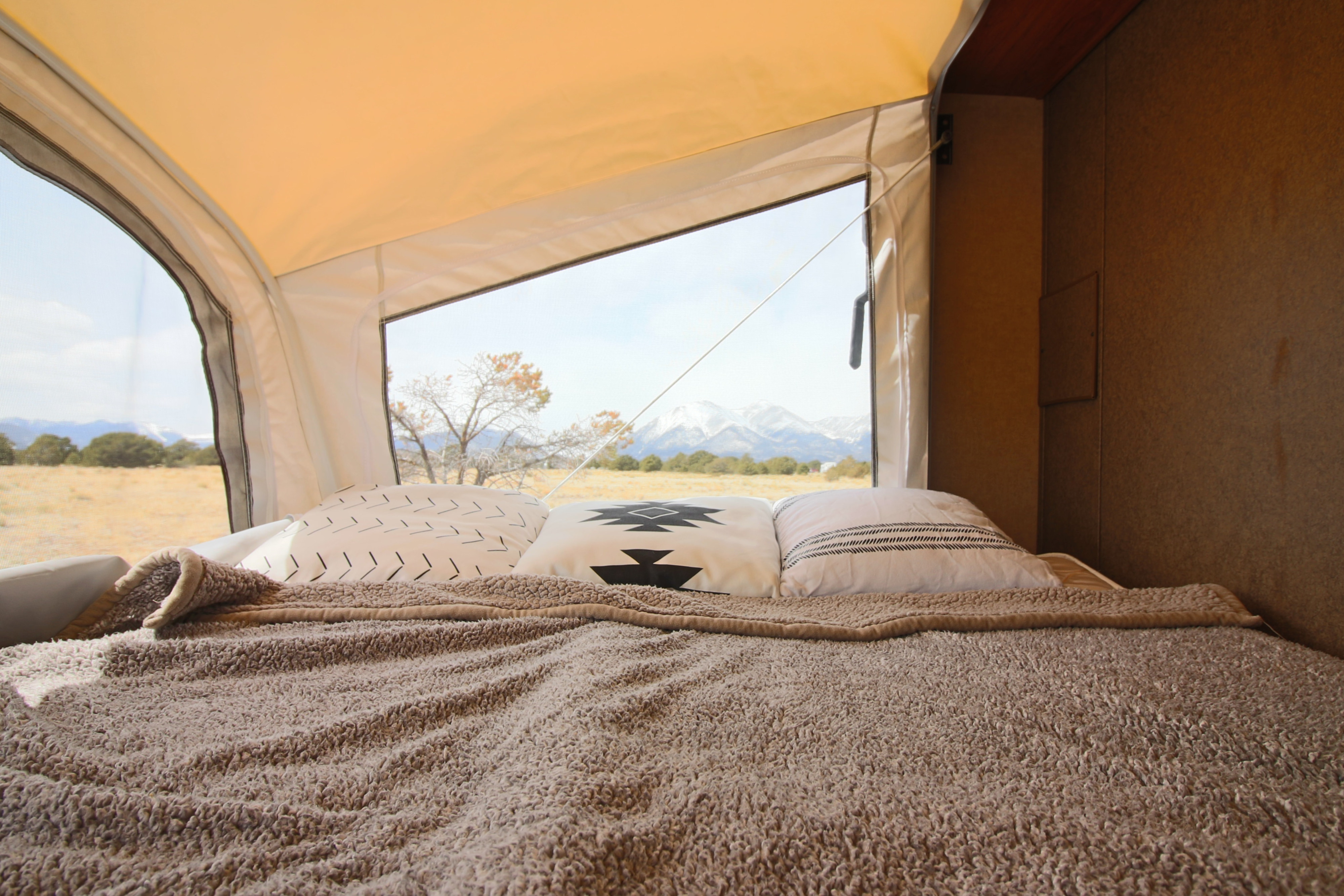 View from inside an RV rental bed, cozy with a fluffy blanket & pillows, overlooking a field and snowy mountains.. Starcraft Launch 2016