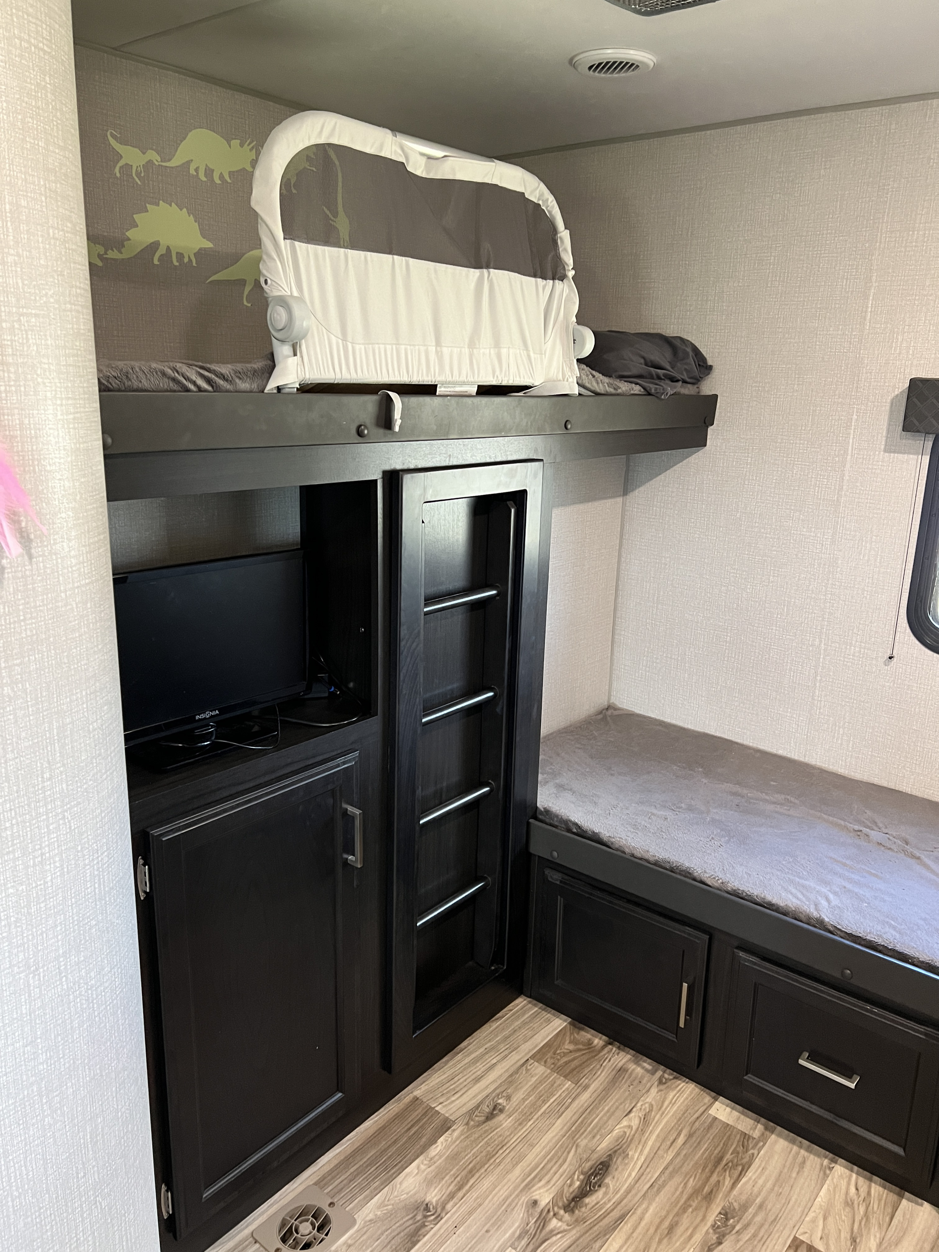 Family-friendly RV rental bunk room with dark cabinetry, built-in TV, a baby sleeper on the top bunk, and playful dinosaur wall art.. Venture Stratus 2020