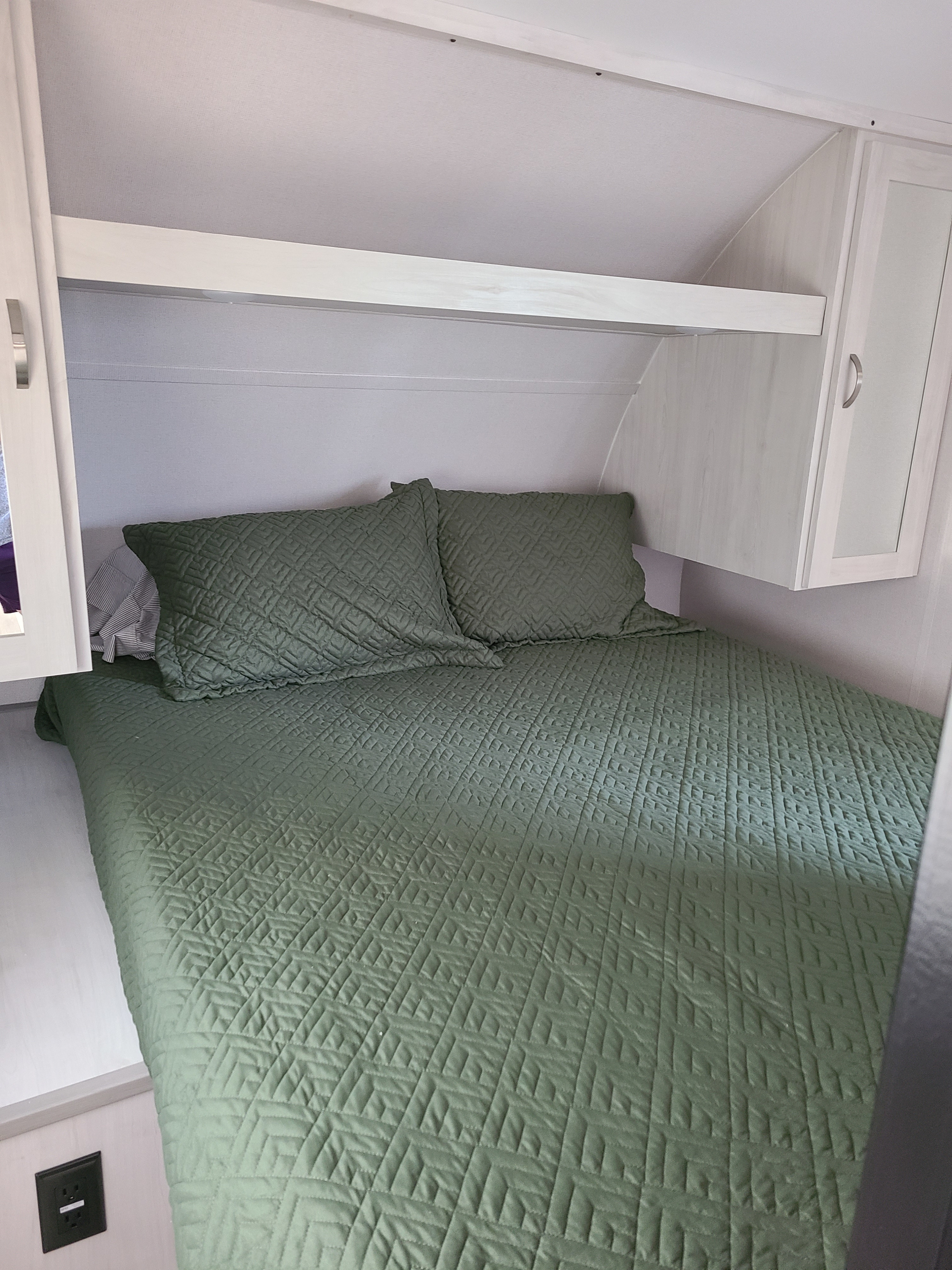 Cozy RV rental bedroom: green quilted bed, pillows, and overhead storage. Ideal for travel trailer adventures.. Forest River Tracer 2021