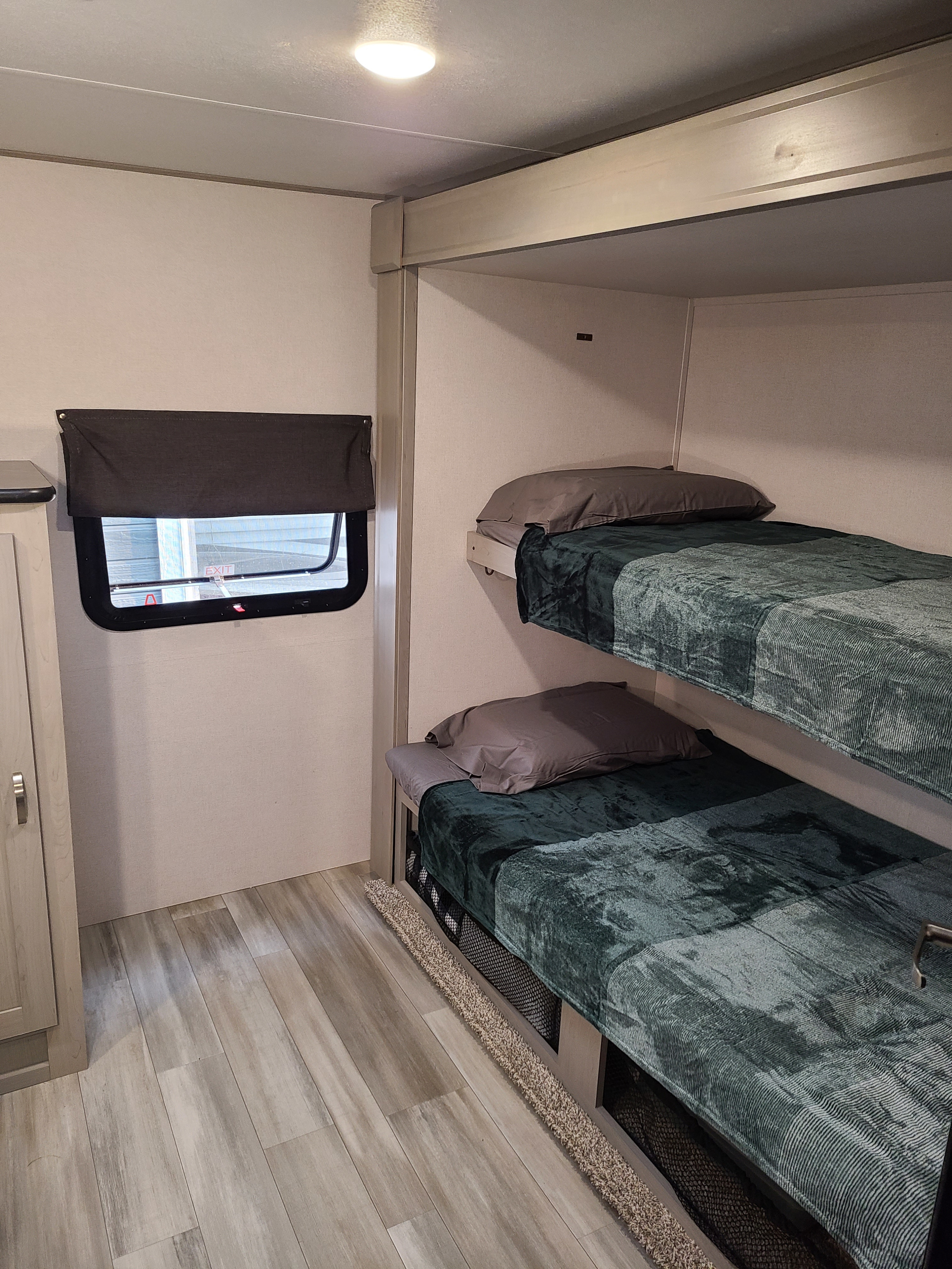 Cozy RV rental interior featuring bunk beds with green blankets, a window, and light wood-look flooring, perfect for travel.. Forest River Tracer 2021