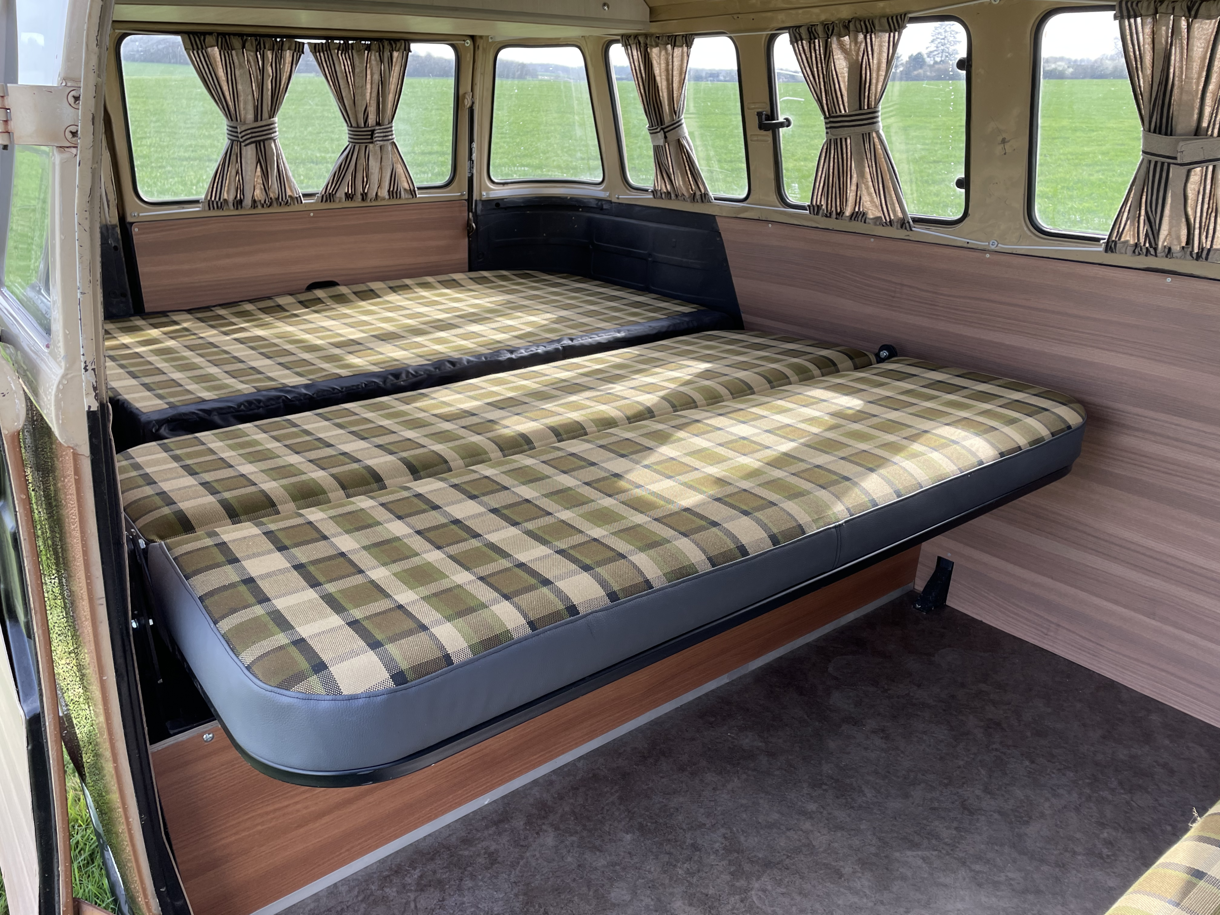 This RV rental offers a cozy interior with two inviting plaid beds, wood-look walls, and scenic window views of a green field.. Volkswagen westfalia 1983