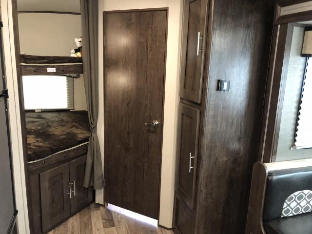 This RV rental interior features dark wood bunk beds, a private door, and built-in storage cabinets. Ideal for families.. Radiance Wolf's Den 2019