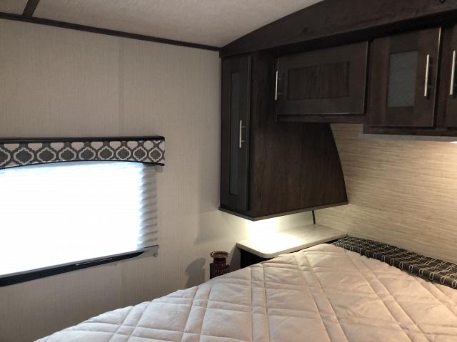 Comfortable RV rental bedroom: quilted bed, window with blinds, and practical overhead storage.. Radiance Wolf's Den 2019