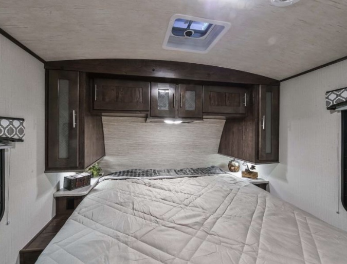 This RV rental bedroom features a comfortable bed, dark wood overhead storage, and accent lighting, perfect for your journey.. Radiance Wild Cat 2018