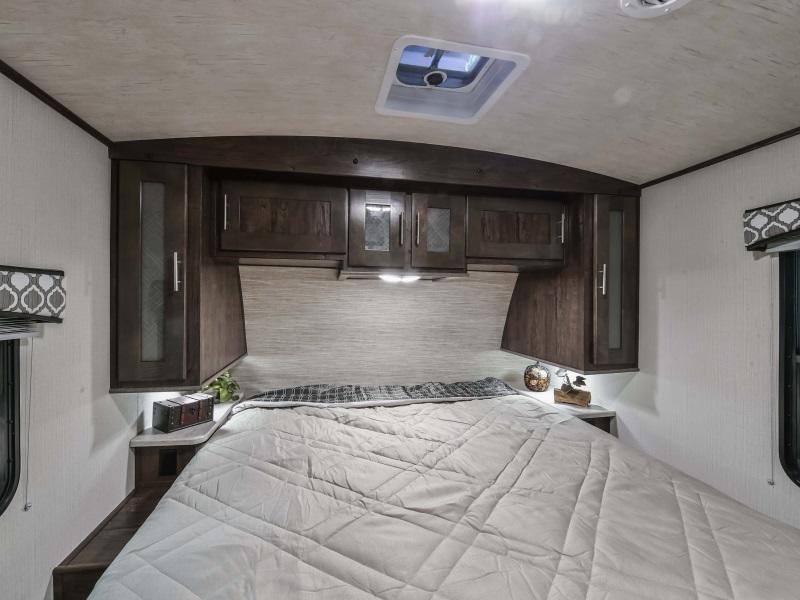 This RV rental bedroom features a queen bed centered under dark wood overhead cabinets. A skylight is visible on the ceiling.. Radiance Big Bear 2020