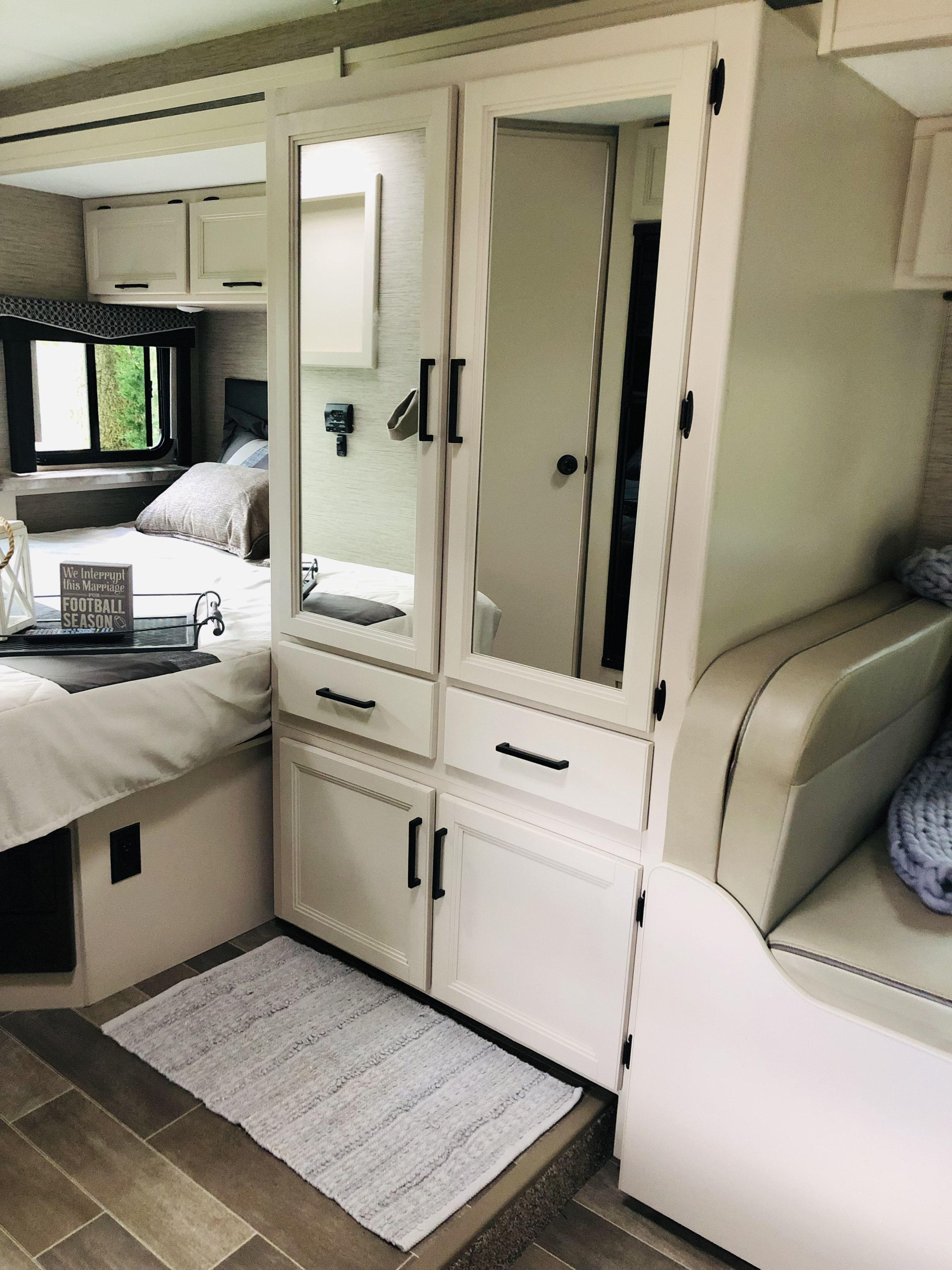 Clean RV rental bedroom interior featuring a comfortable bed, integrated mirrored storage, and cozy seating.. Thor Chateau 2022