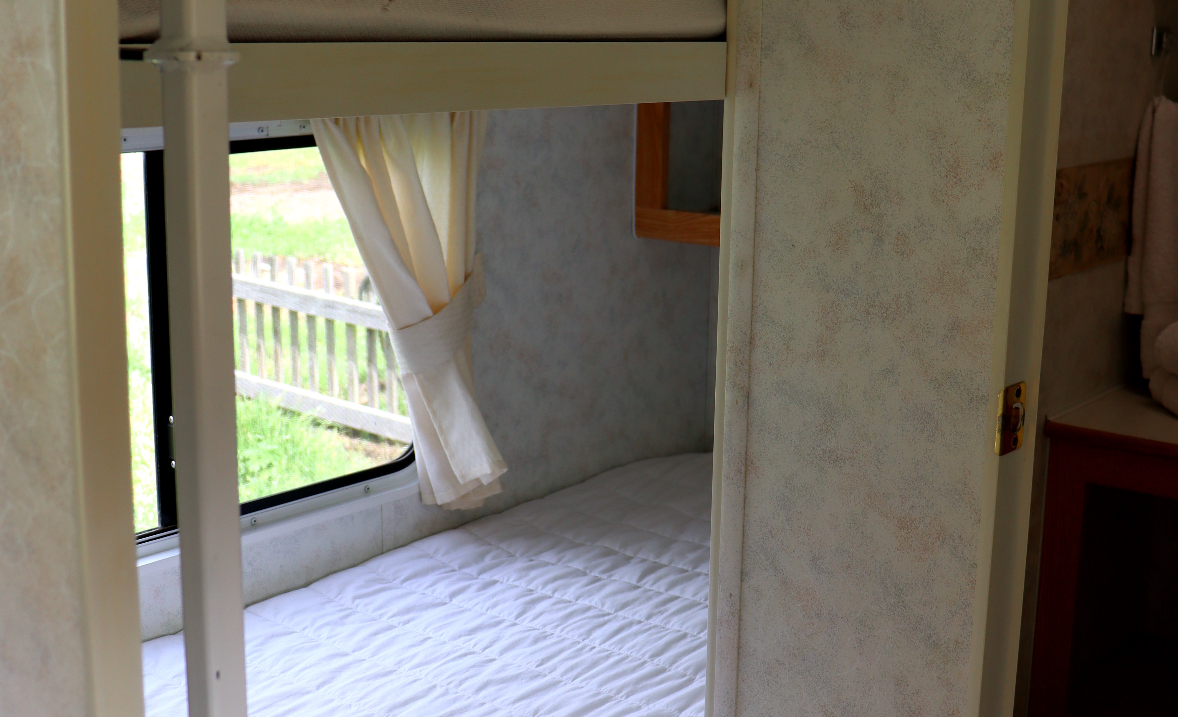 Cozy bunk bed area inside an RV rental, offering a comfortable stay with a scenic window view of nature.. Komfort Komfort Trailer 2003
