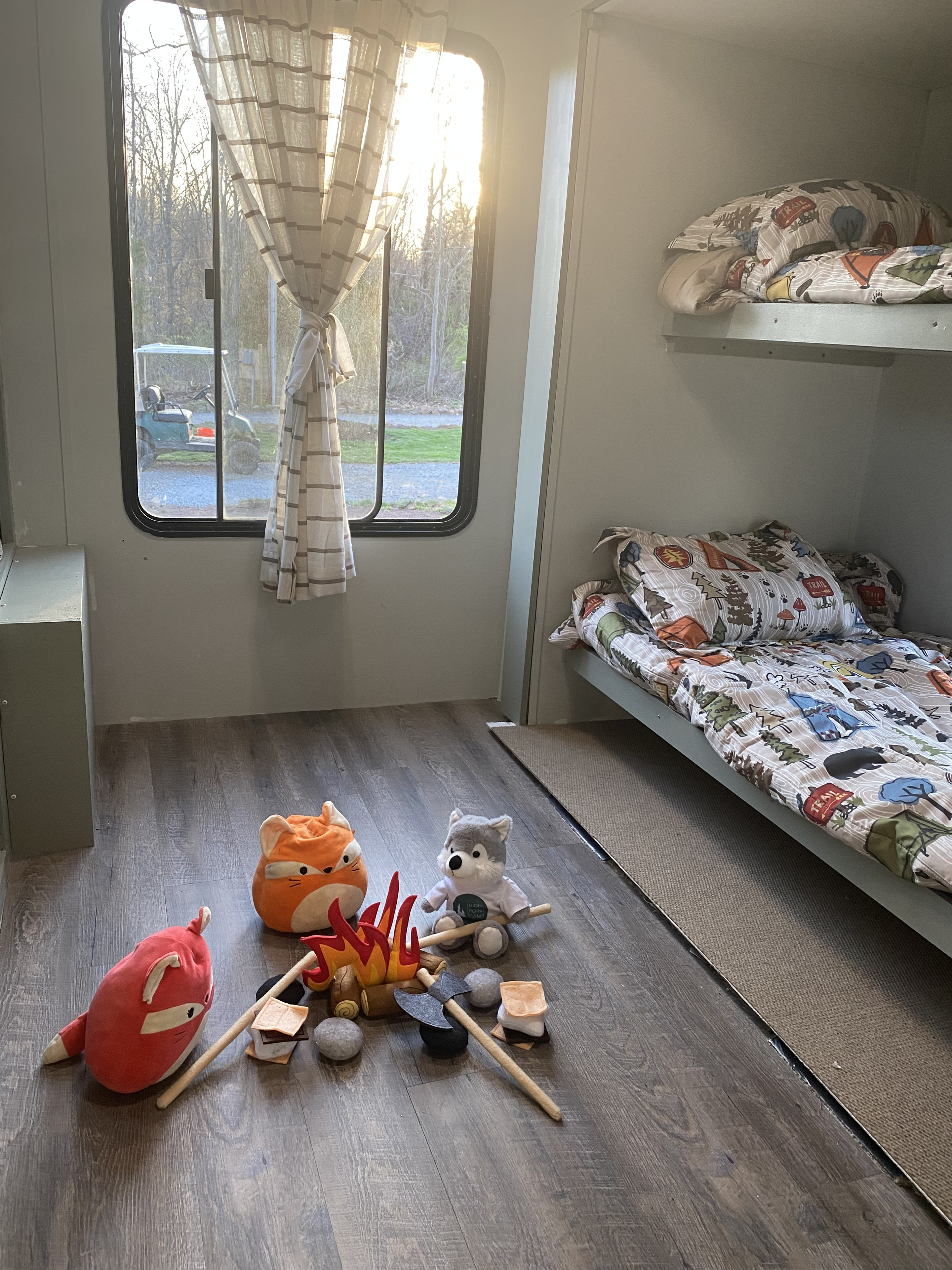 RV rental interior: cozy bunk beds with camping bedding, sunlit window, and playful stuffed animals by a pretend campfire.. Gulf Stream Conquest 2015