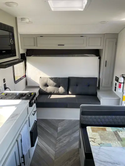 Bright RV rental interior showcasing a kitchen with stovetop, microwave, comfy sofa, and dining space.. Forest River Wildwood FSX 179DBK 2022