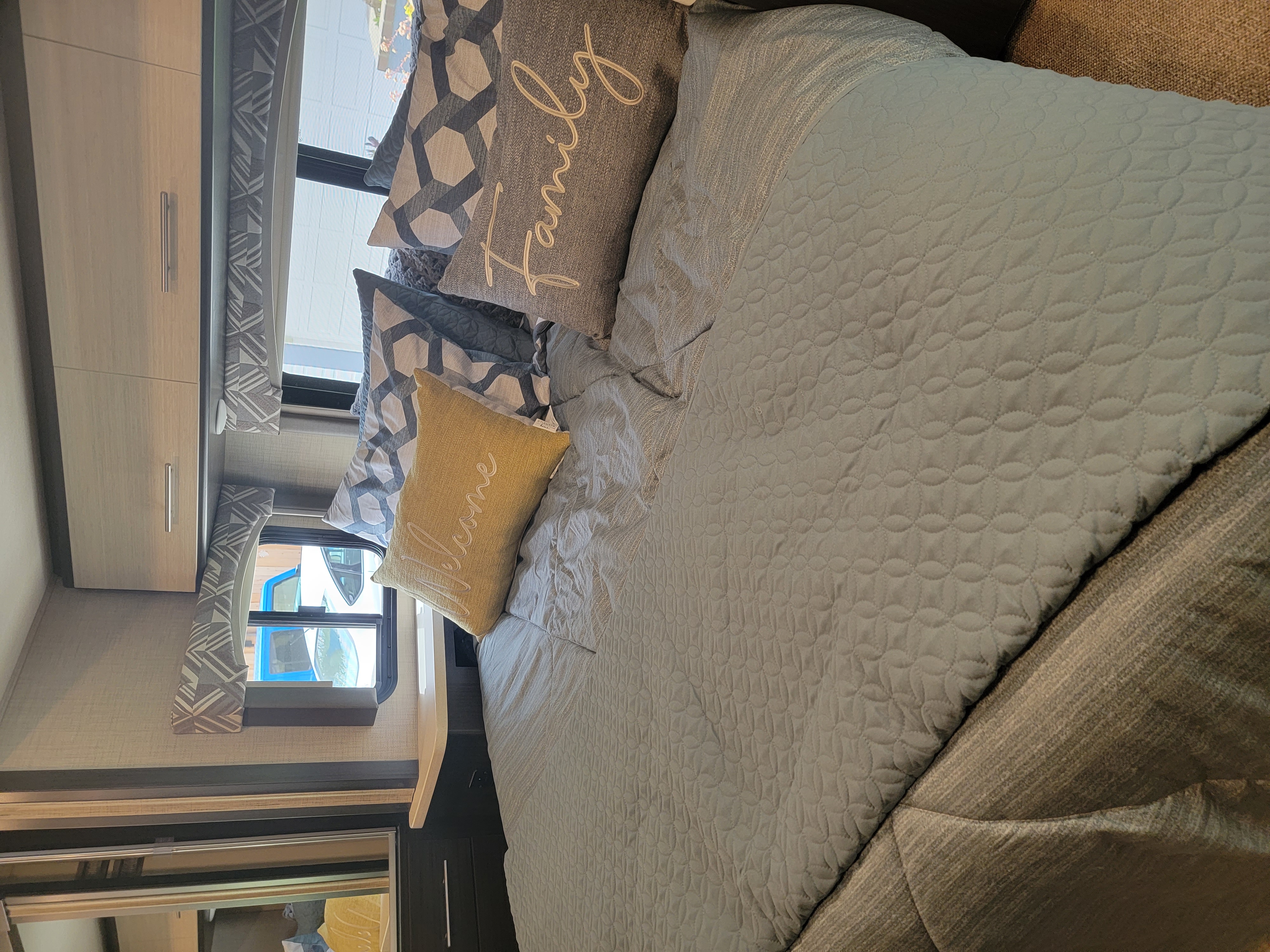 Experience comfort in this inviting RV rental bedroom. Features quilted bedding, decorative pillows, and stylish decor.. Thor Axis 2021