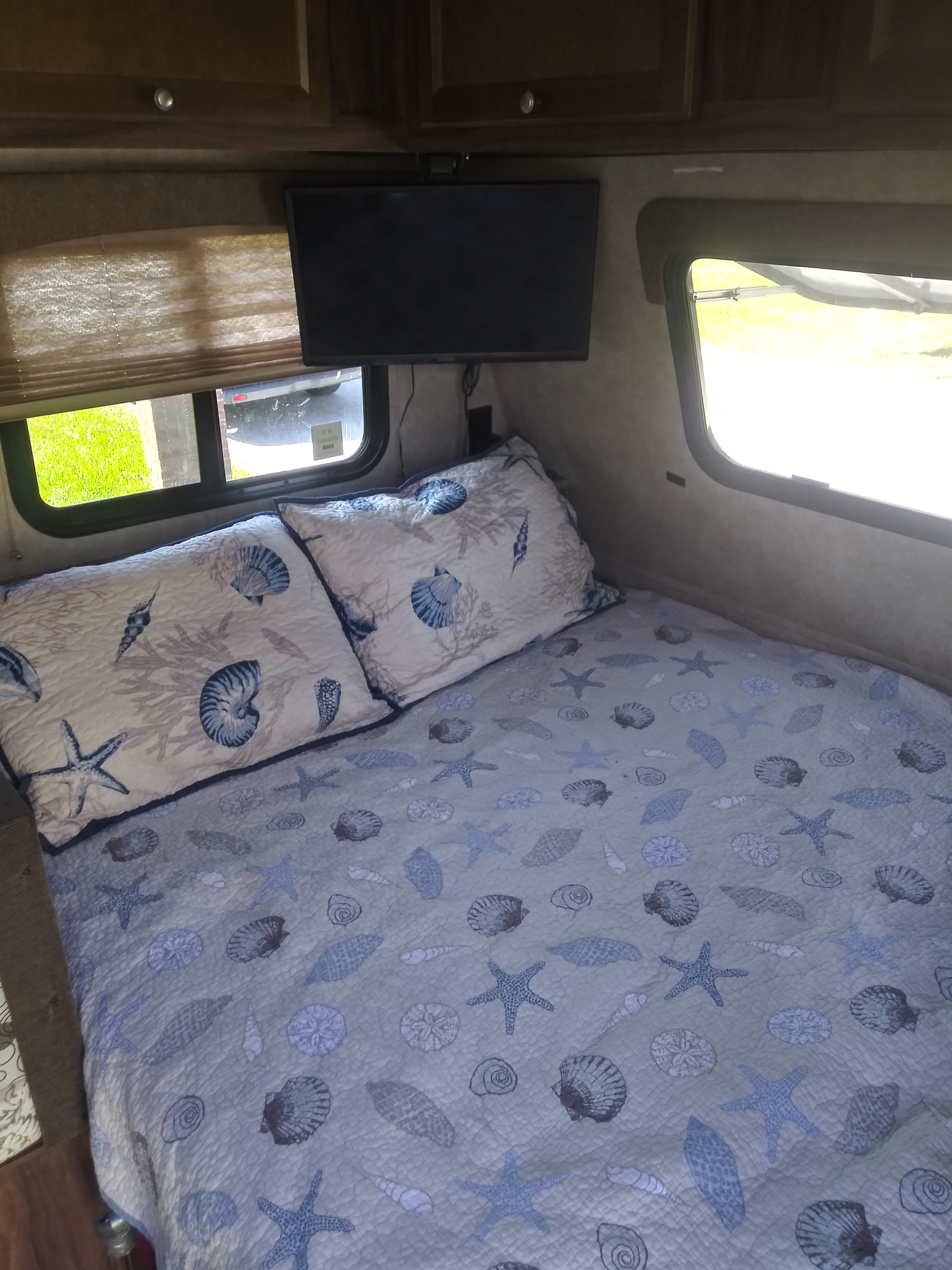 Cozy rv rental bedroom with seashell quilt, pillows, and TV, offering a view of nature outside.. Coachmen Clipper 2016