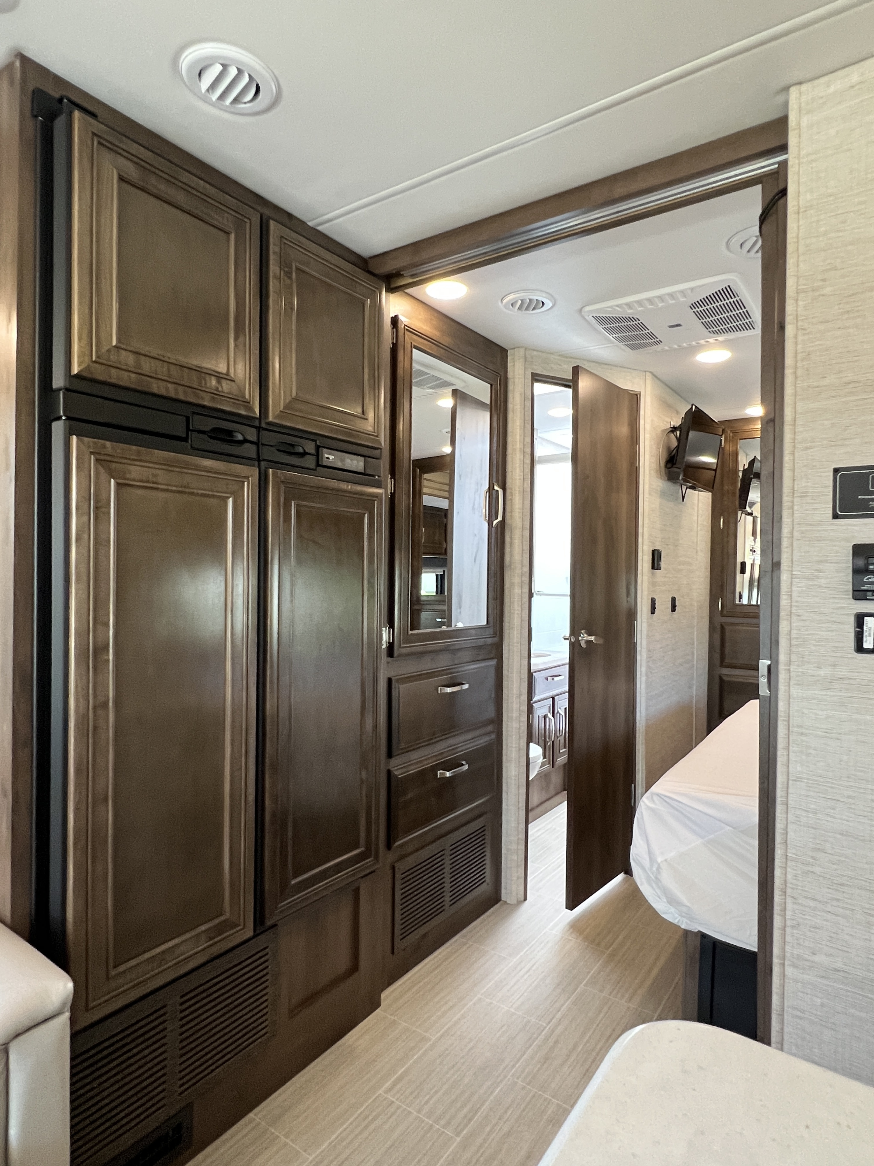 Inside a modern RV rental: dark wood cabinetry, a functional hallway leading to a cozy bedroom and bathroom.. Entegra Coach Esteem 2022