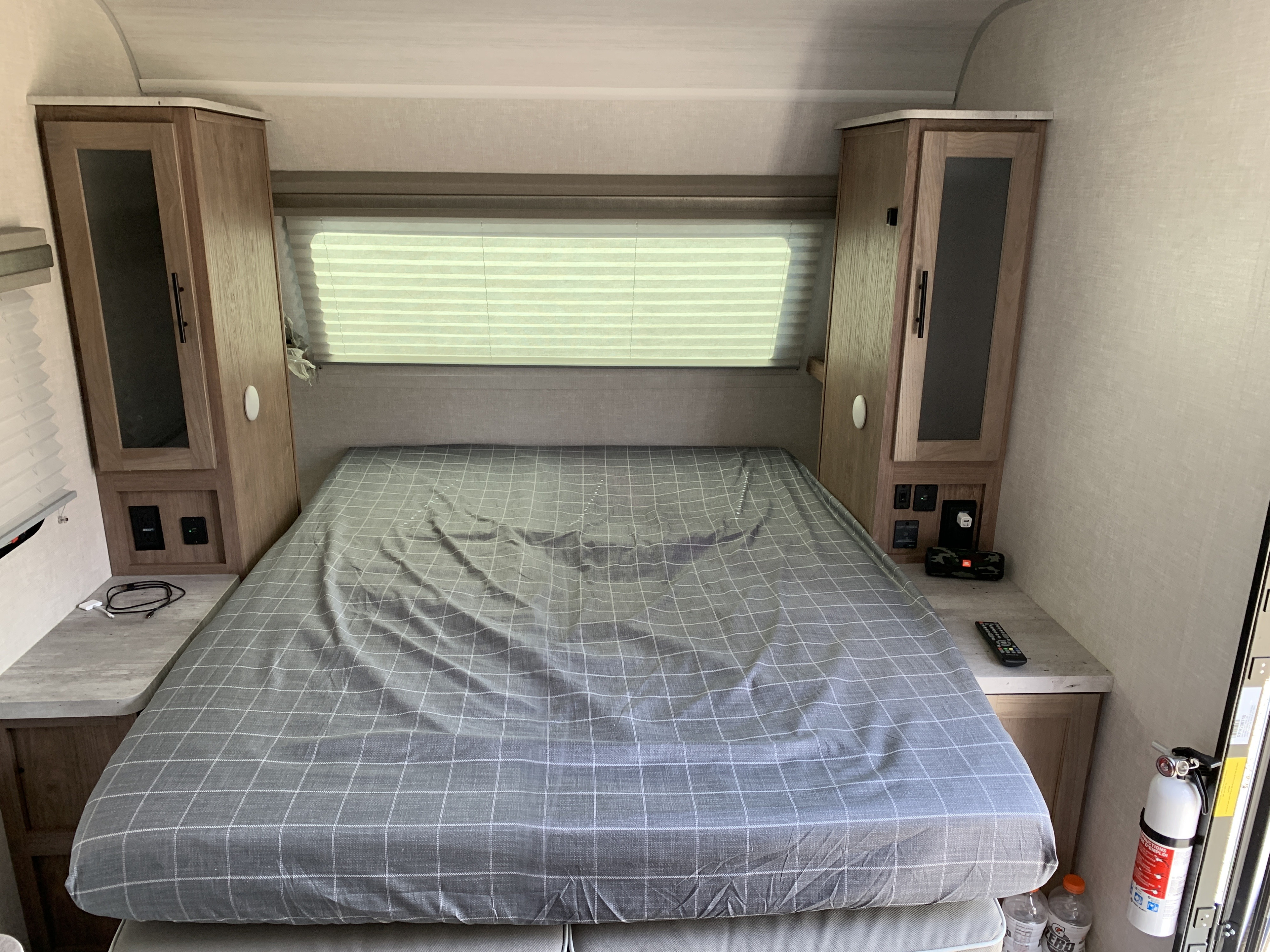RV rental bedroom: a bed with plaid sheet, side cabinets, window, charging access, and fire extinguisher visible.. Forest River No Boundries 19.3 2022