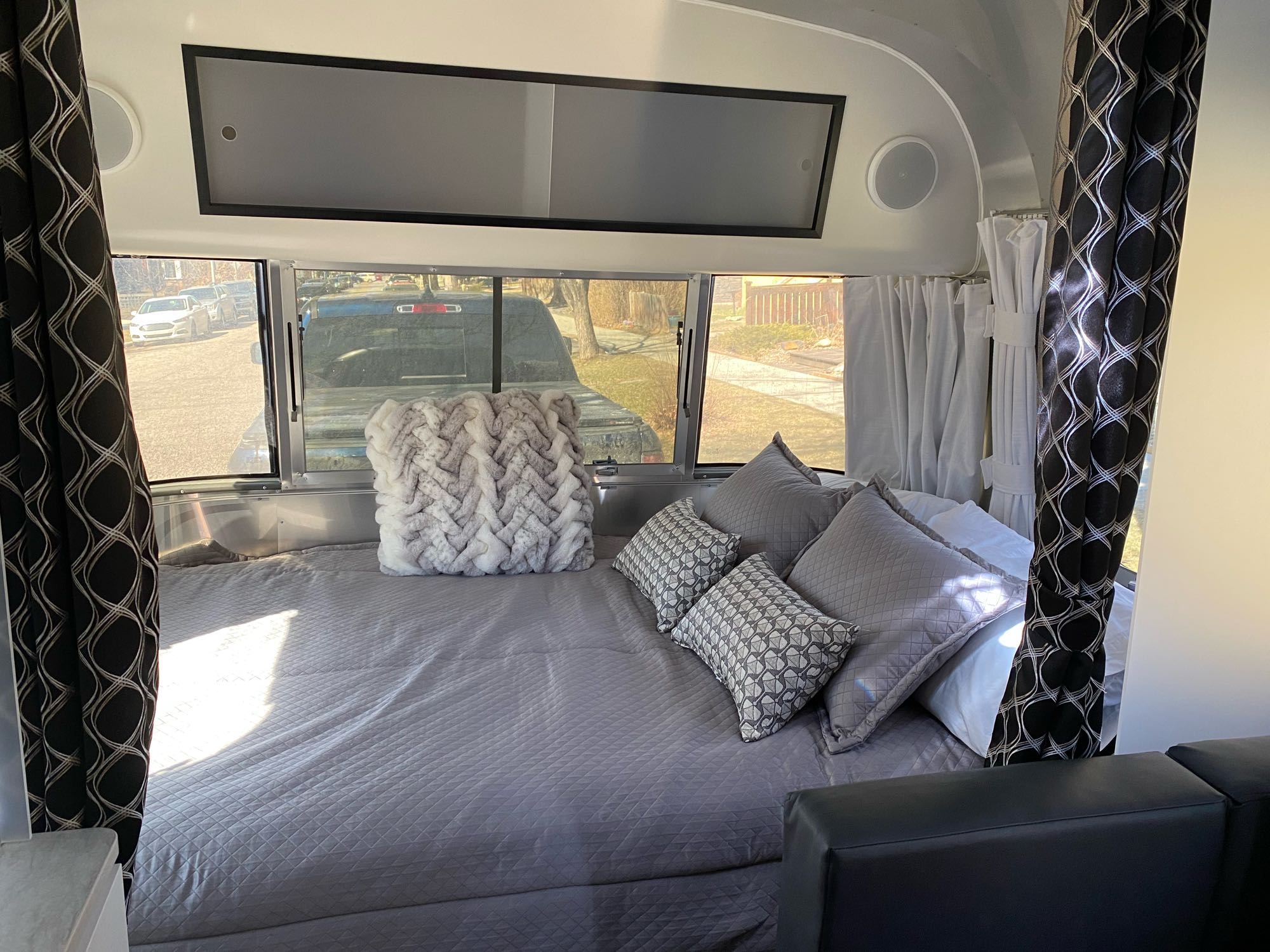 RV rental bedroom: a cozy space with a large bed, grey bedding, patterned pillows, and dark curtains.. Airstream Caravel 2022
