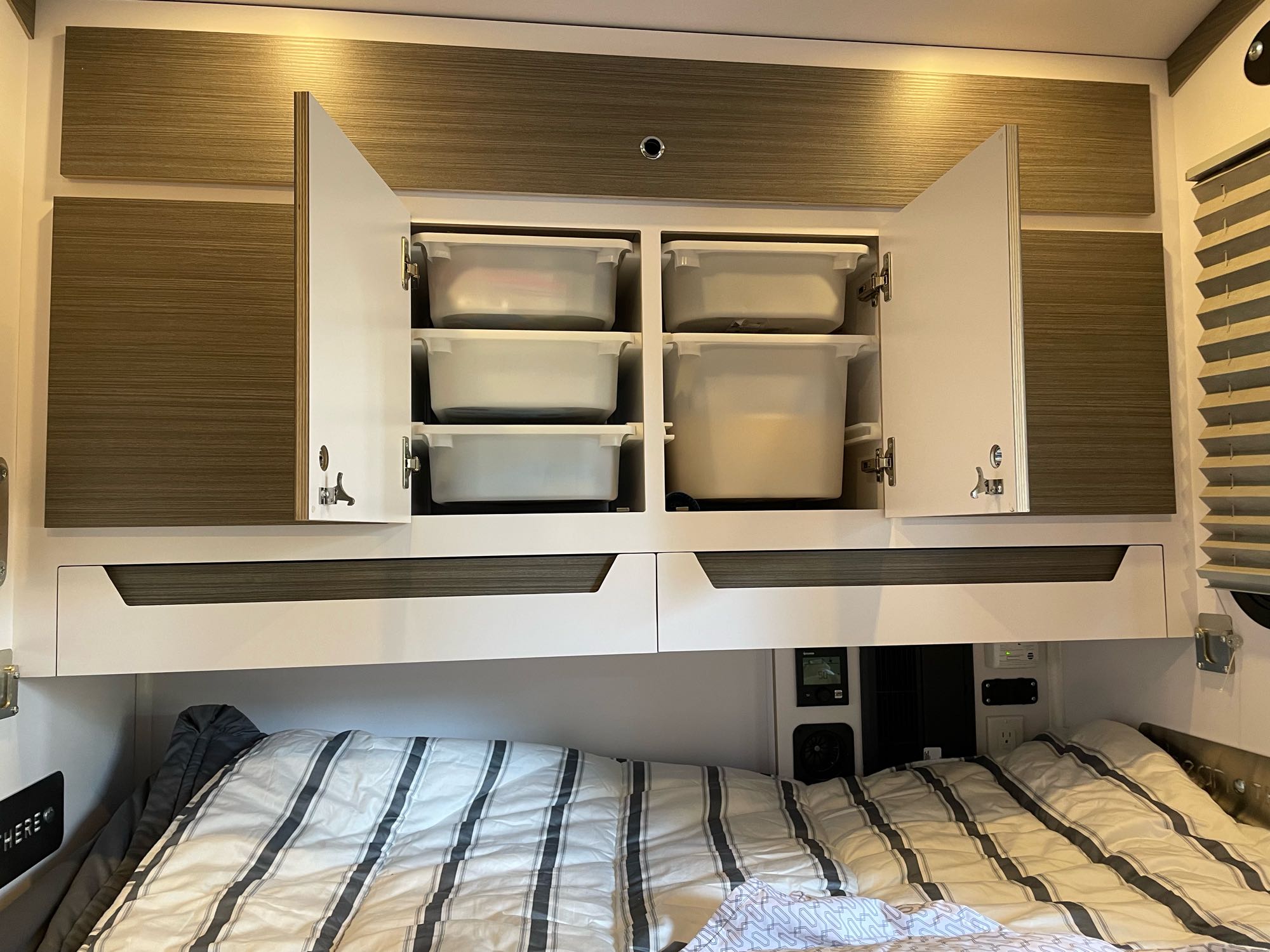 Organized RV rental bedroom with striped bed, open overhead cabinets revealing storage bins, and modern finishes.. Bean Mean Bean 2022