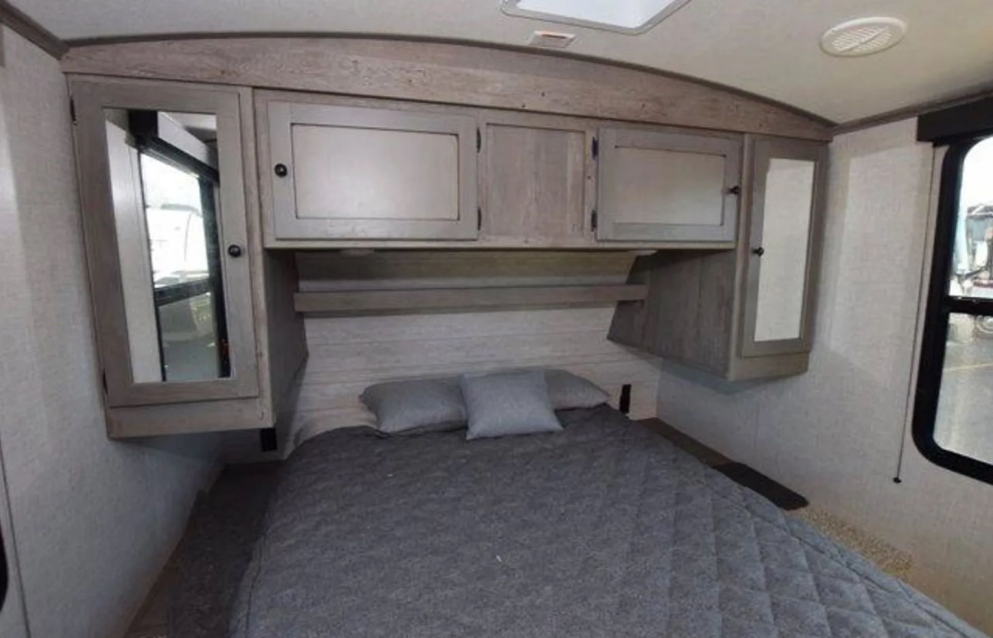 Comfortable RV rental bedroom featuring a grey quilted bed, overhead cabinets, and mirrored wardrobes for travel.. Keystone RV Outback Ultra-Lite 2020