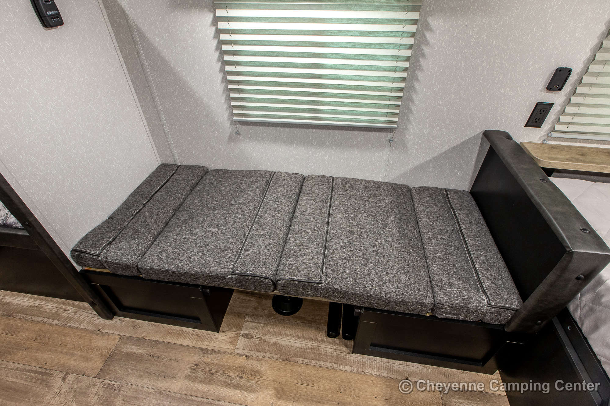 Inside an RV rental: a gray cushioned bench-style seating area with storage, convertible to a bed, plus blinds and outlets.. Forest River Cherokee Wolf Pup 2022