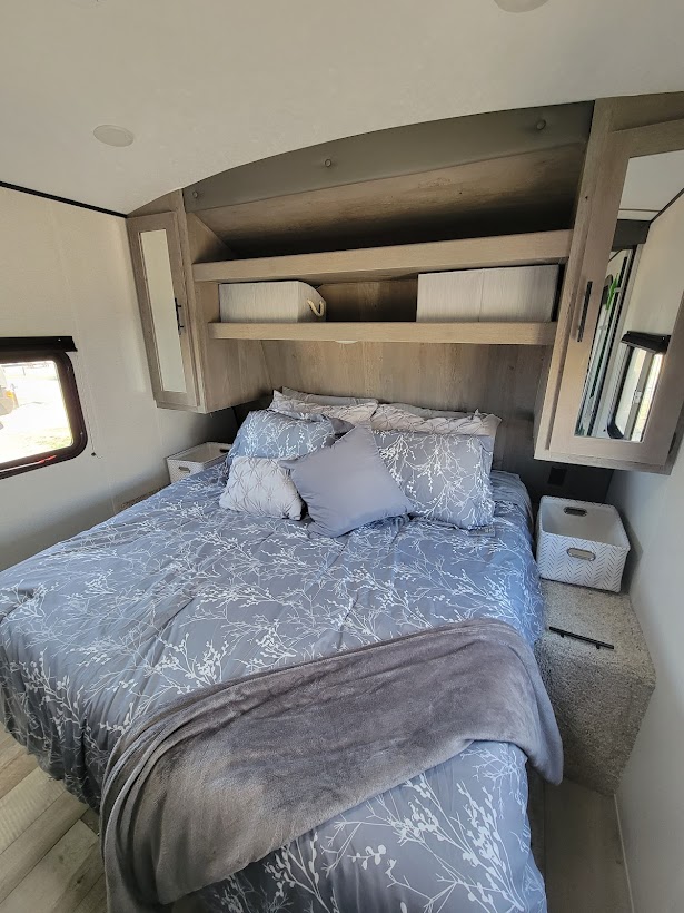 Cozy RV rental bedroom featuring patterned bedding, overhead storage, and thoughtful design for comfortable travel accommodation.. Keystone RV Springdale 2021