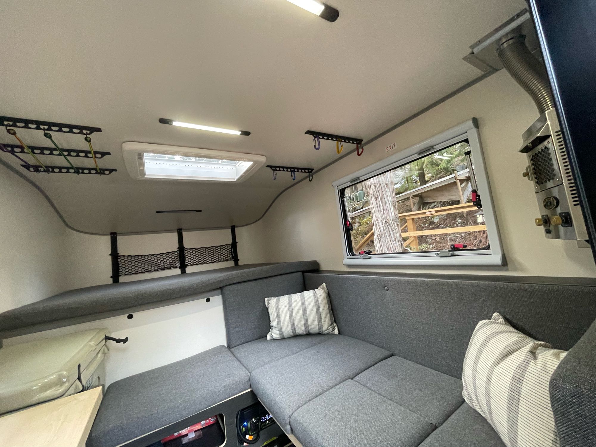Cozy RV rental interior with L-shaped cushioned seating, window view, skylight, and practical ceiling storage/drying racks.. Ford Ranger 2021