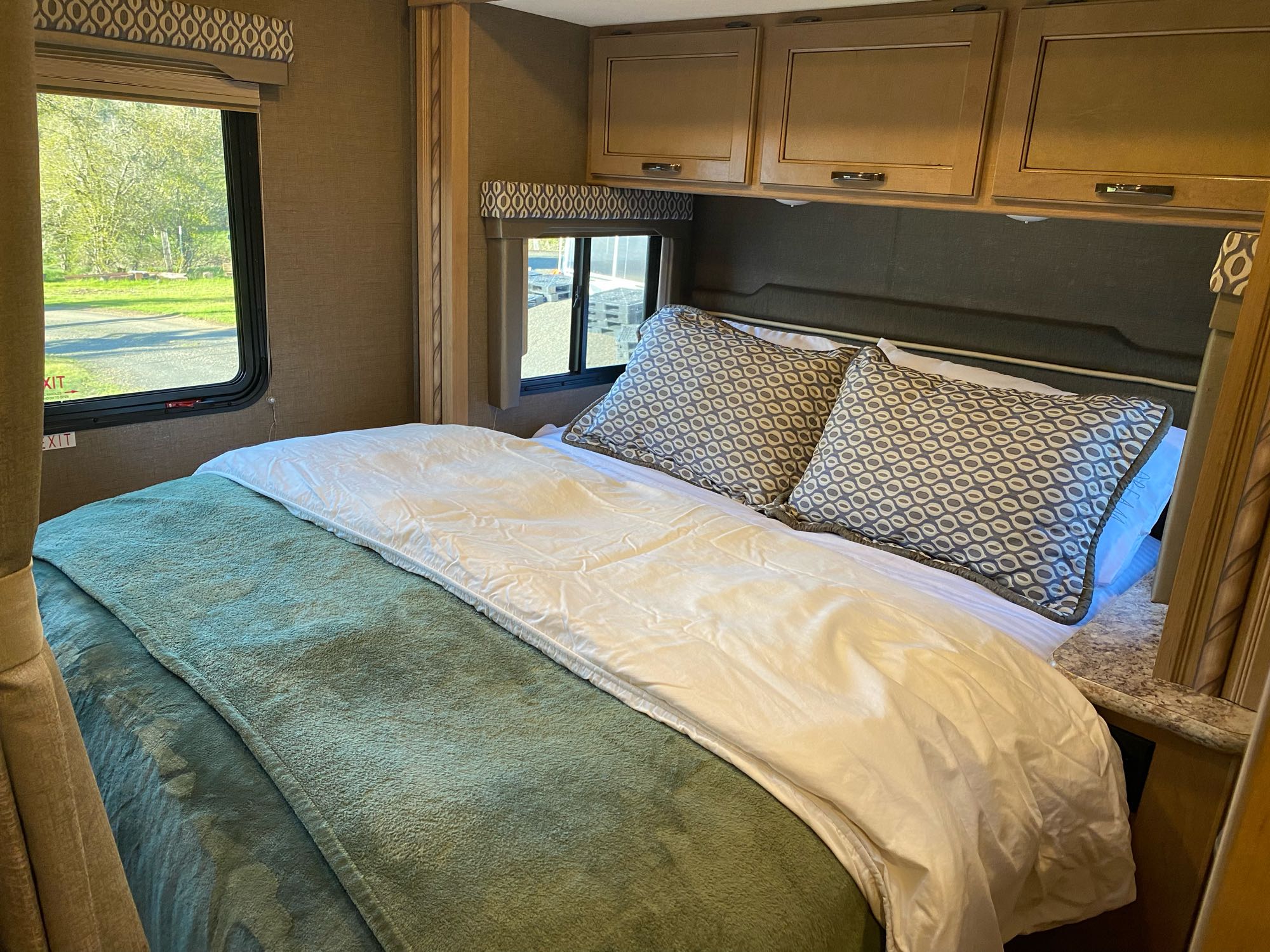Comfortable RV rental bedroom featuring a bed with patterned pillows, green blanket, and a large window.. Thor Freedom Elite 2017