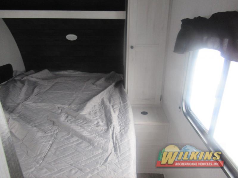 Cozy RV bedroom with a light grey bed, dark paneling, and white cabinets by a bright window. Ideal for your rv rental adventure.. Heartland Trailrunner 2022