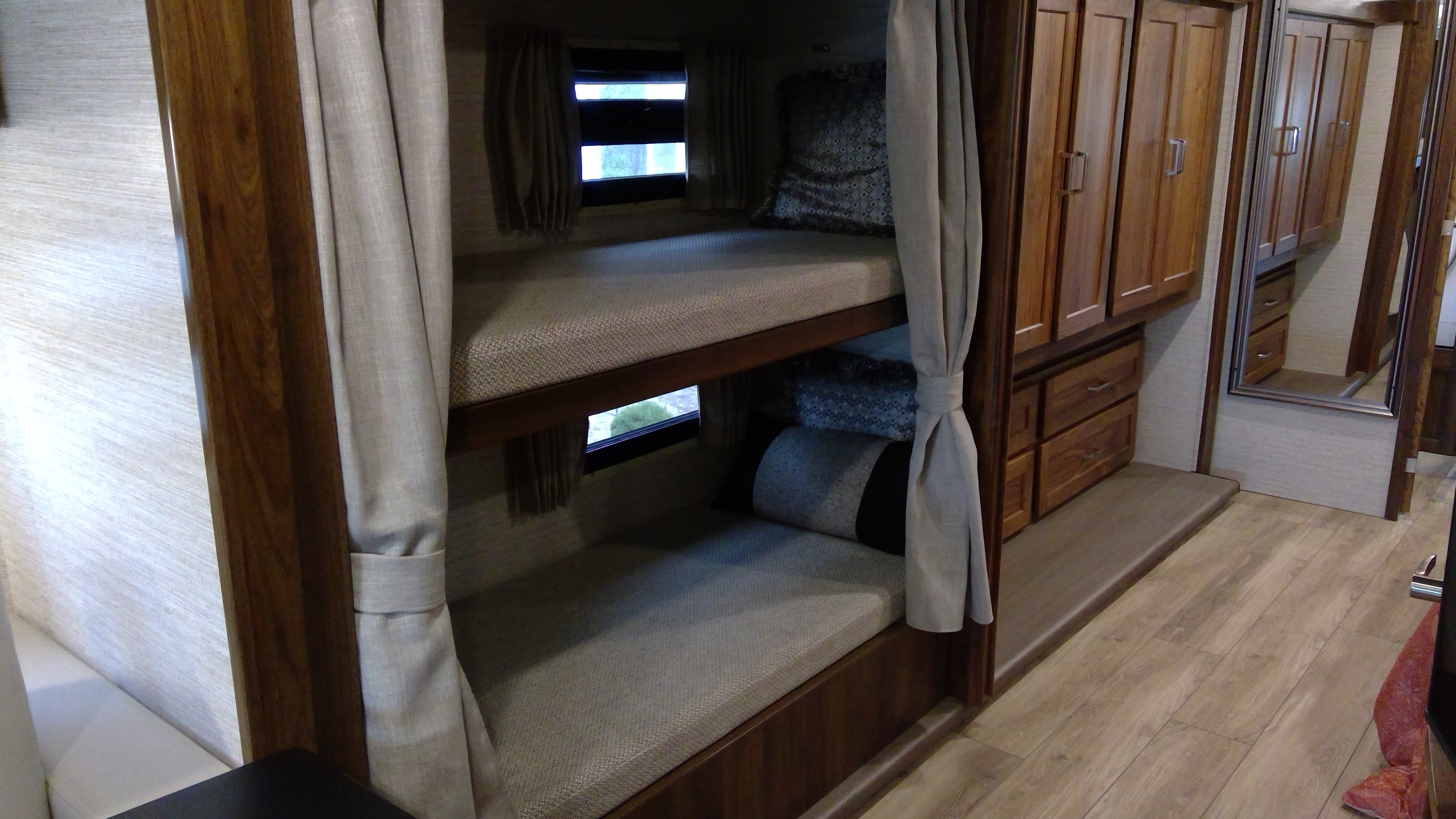 RV rental interior features cozy bunk beds with curtains, ample wood cabinetry, and durable wood-look flooring for travel comfort.. Winnebago Forza 2022