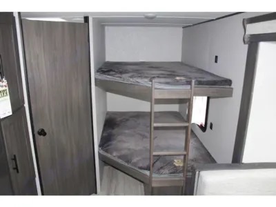Inside this RV rental: cozy bunk beds with dark grey bedding, a ladder, and a wooden door. Ideal for your next family road trip.. Other Other 2021