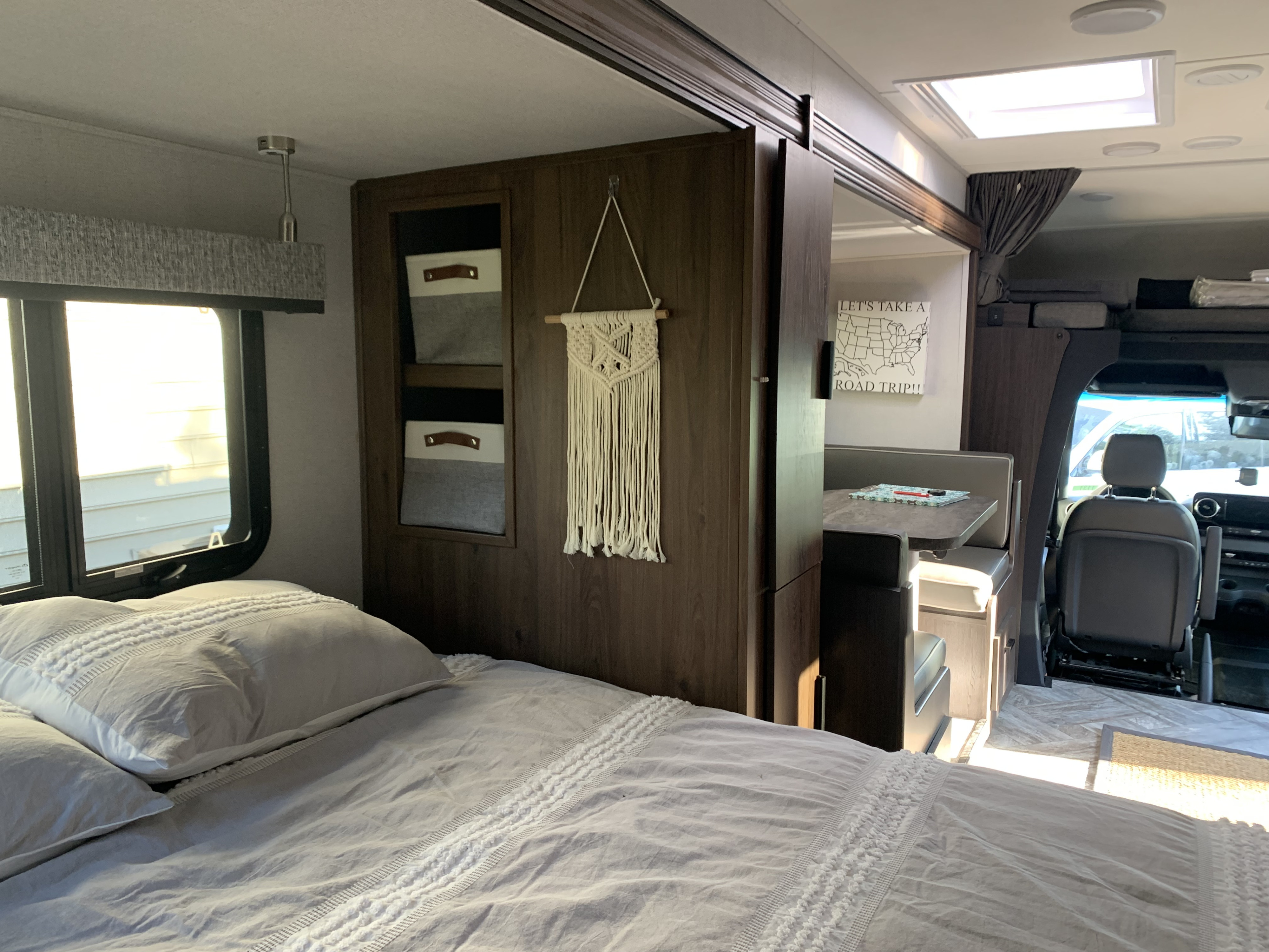 RV rental interior features a cozy bed, macrame decor, dining booth, and driver's area for your next road trip.. Forest River Sunseeker 2022