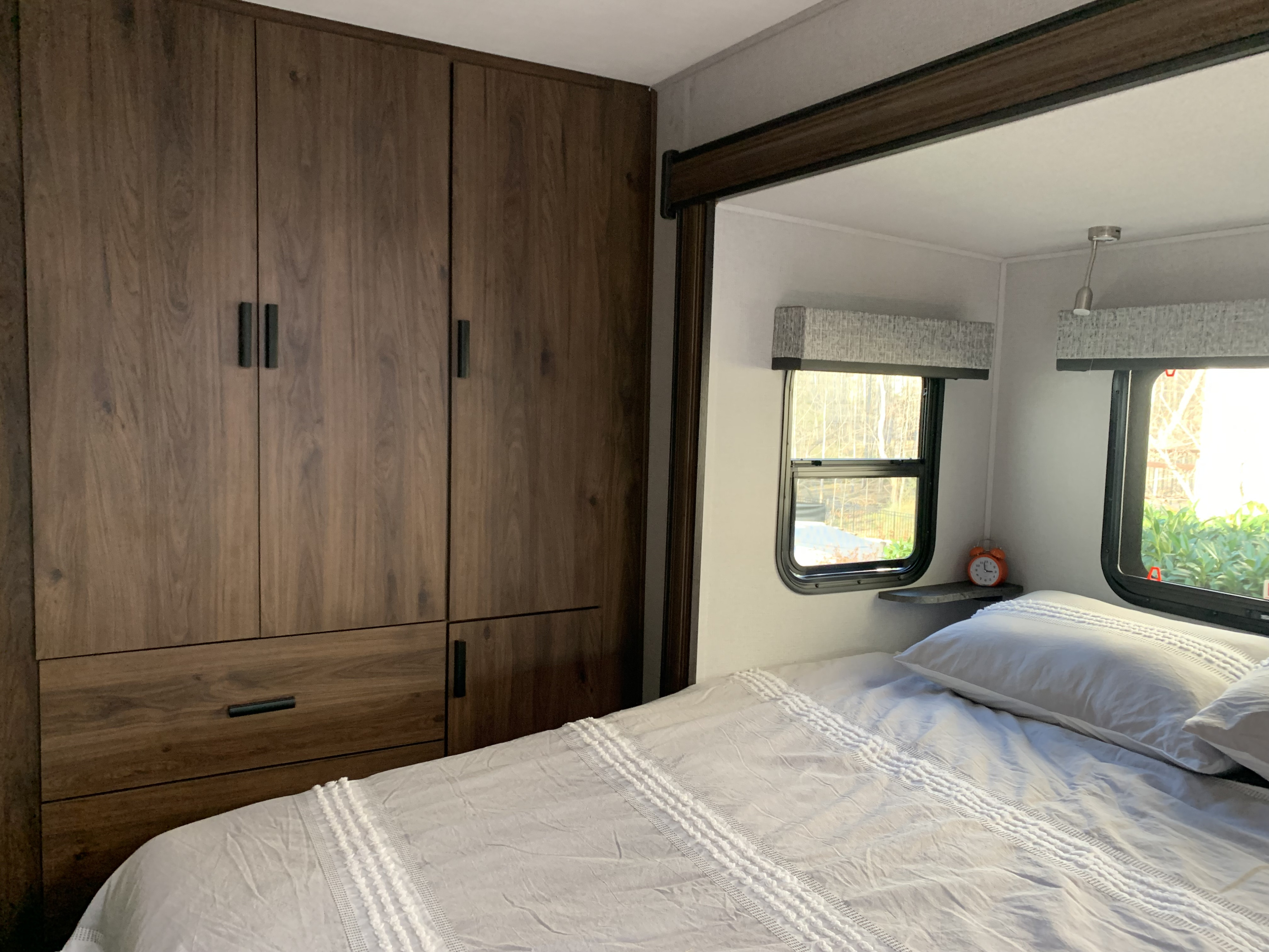 Interior view of an RV rental bedroom with dark wood cabinets, a light gray bed, and bright windows.. Forest River Sunseeker 2022