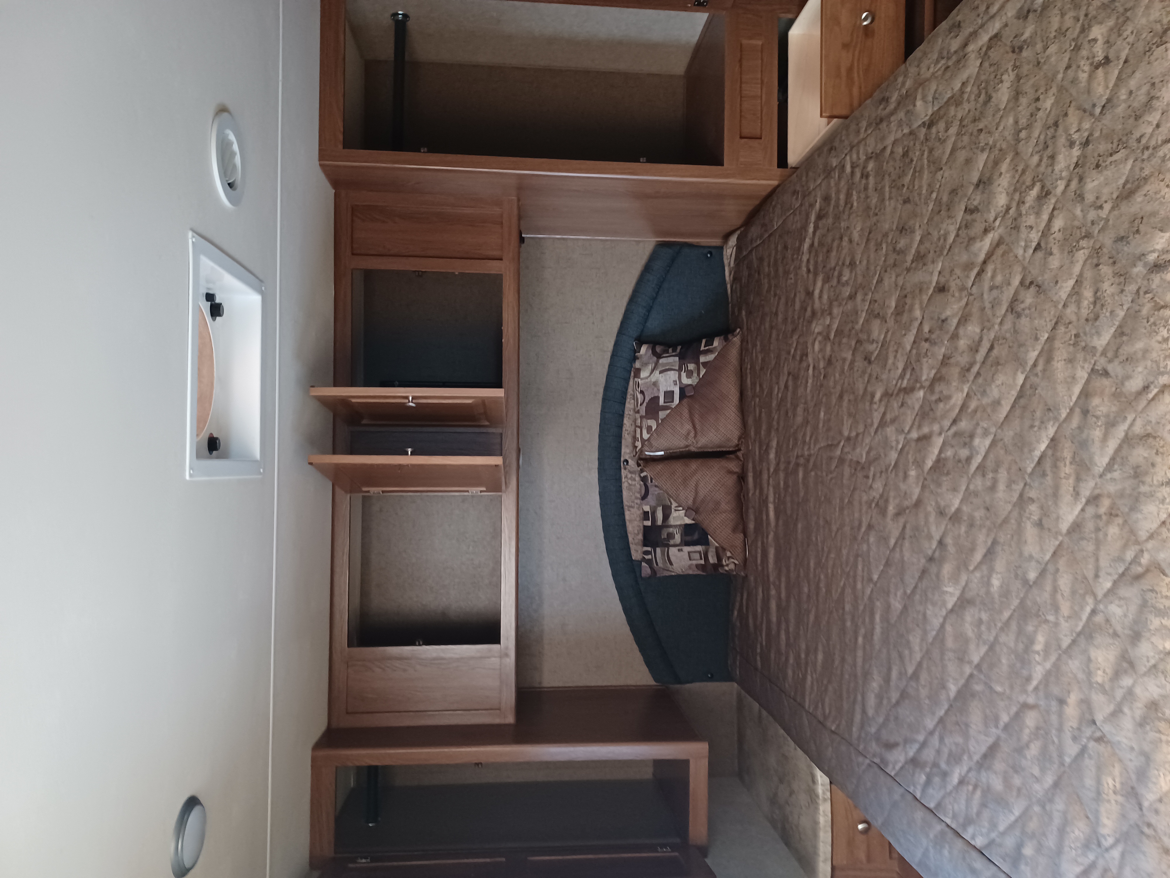 Cozy RV rental bedroom with quilted bedding, patterned pillows, wood cabinetry, and a light-colored wall.. Forest River Coachmen Leprechaun 2016