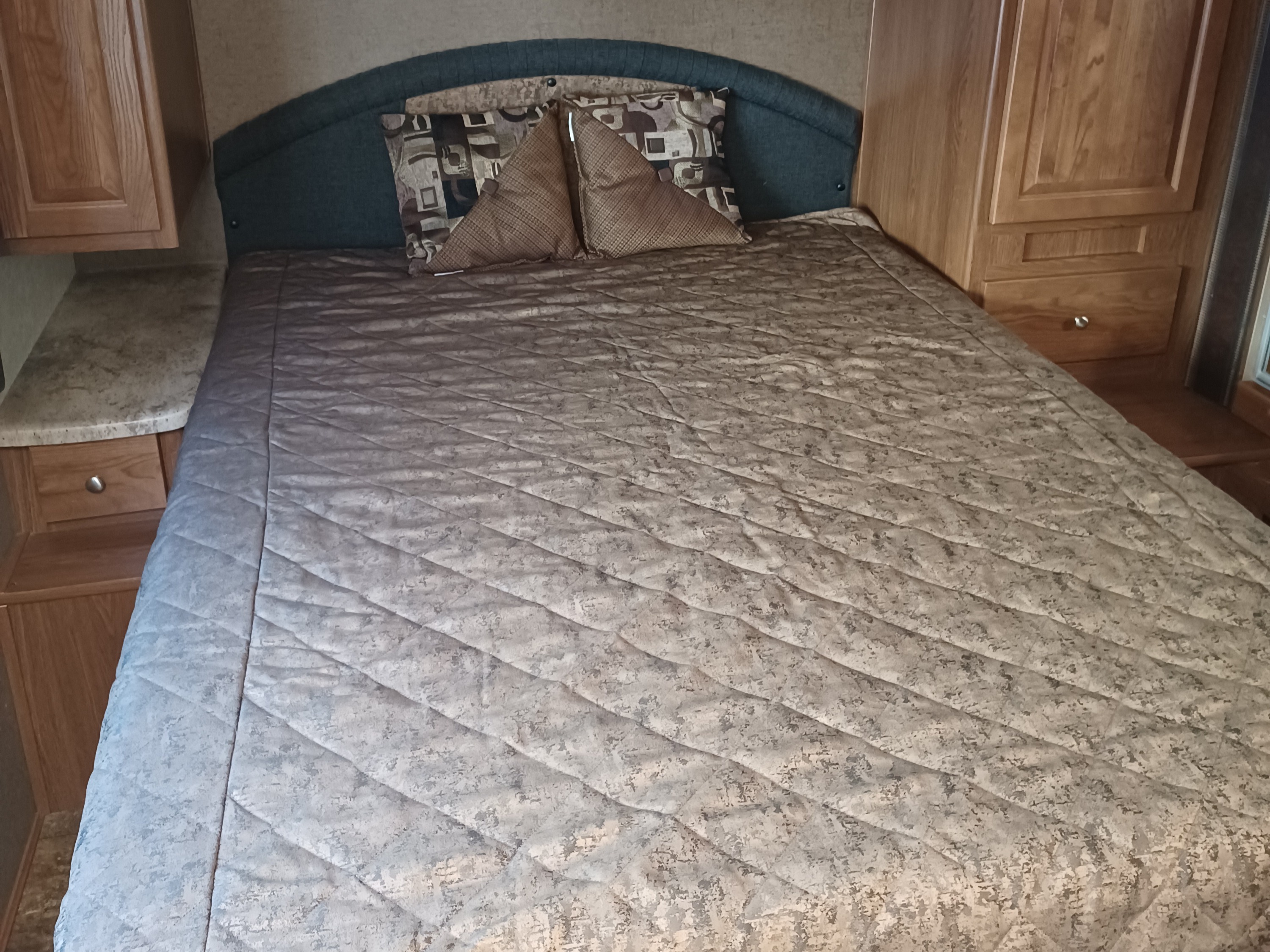 Comfortable RV rental bedroom featuring a quilted bed, headboard, and ample wood storage.. Forest River Coachmen Leprechaun 2016