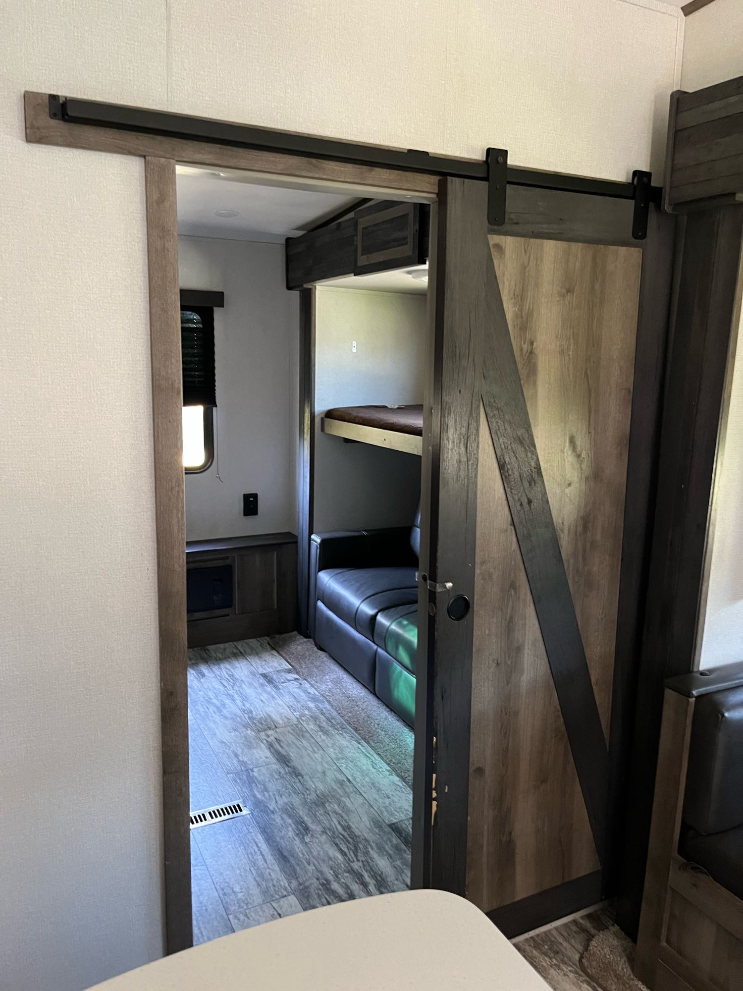 This RV rental interior features a modern barn door slid open, revealing bunk beds, a black sofa, and wood-look flooring.. Keystone RV Sprinter Limited 2021